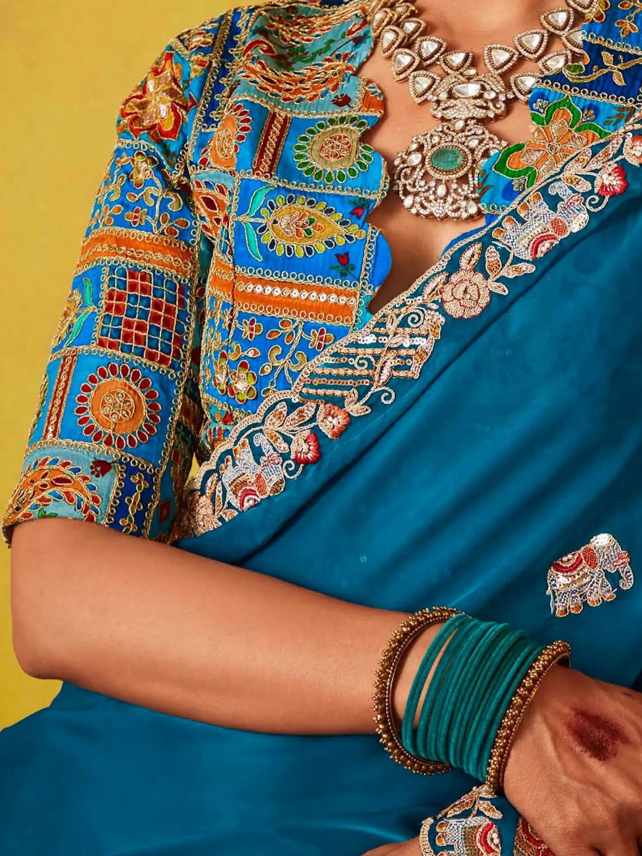 Blue embroidered saree with floral and elephant motifs, paired with statement jewelry and bangles