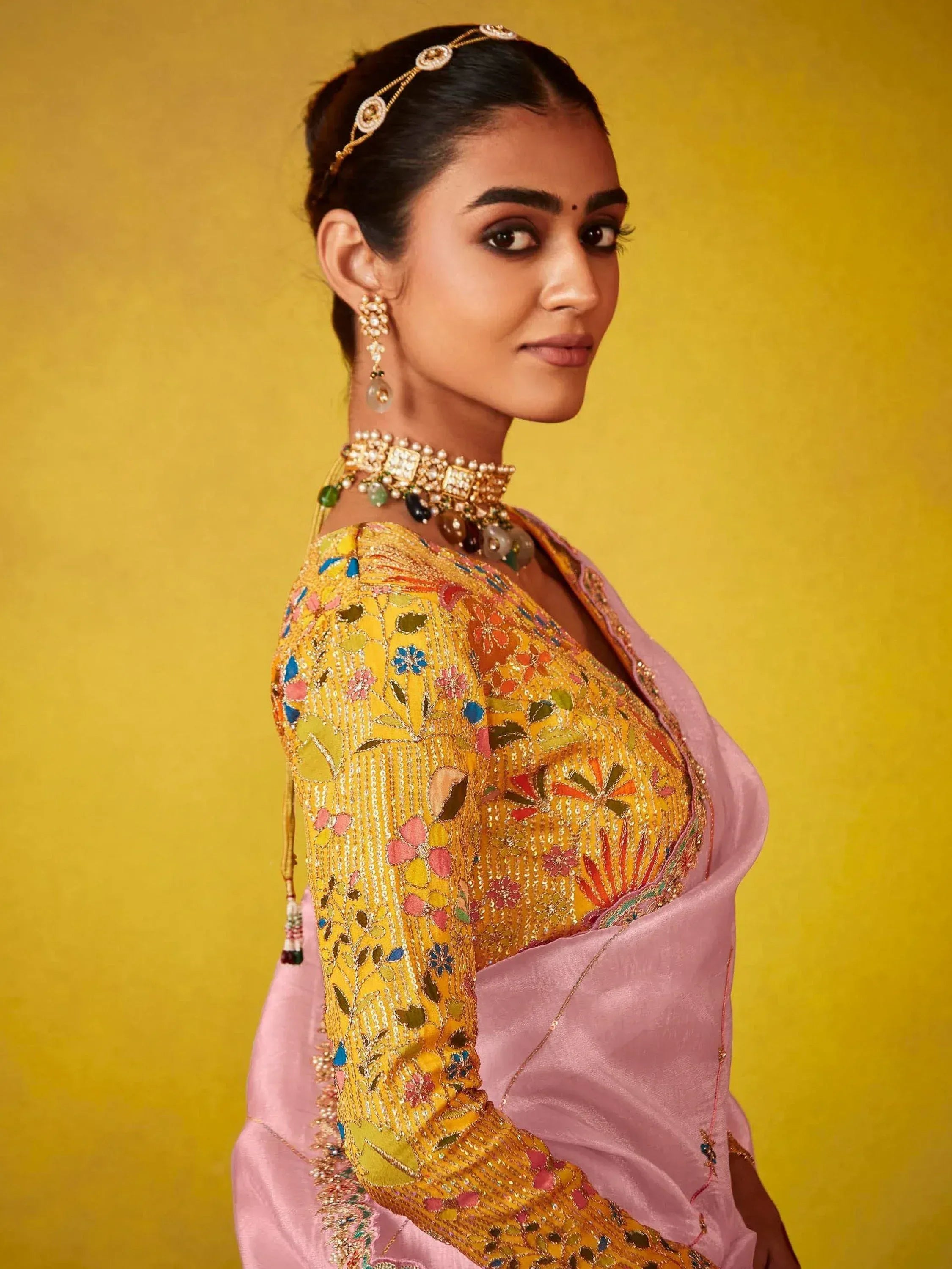 Woman in floral embroidered yellow blouse with pink saree, traditional Indian ethnic wear, gold jewelry
