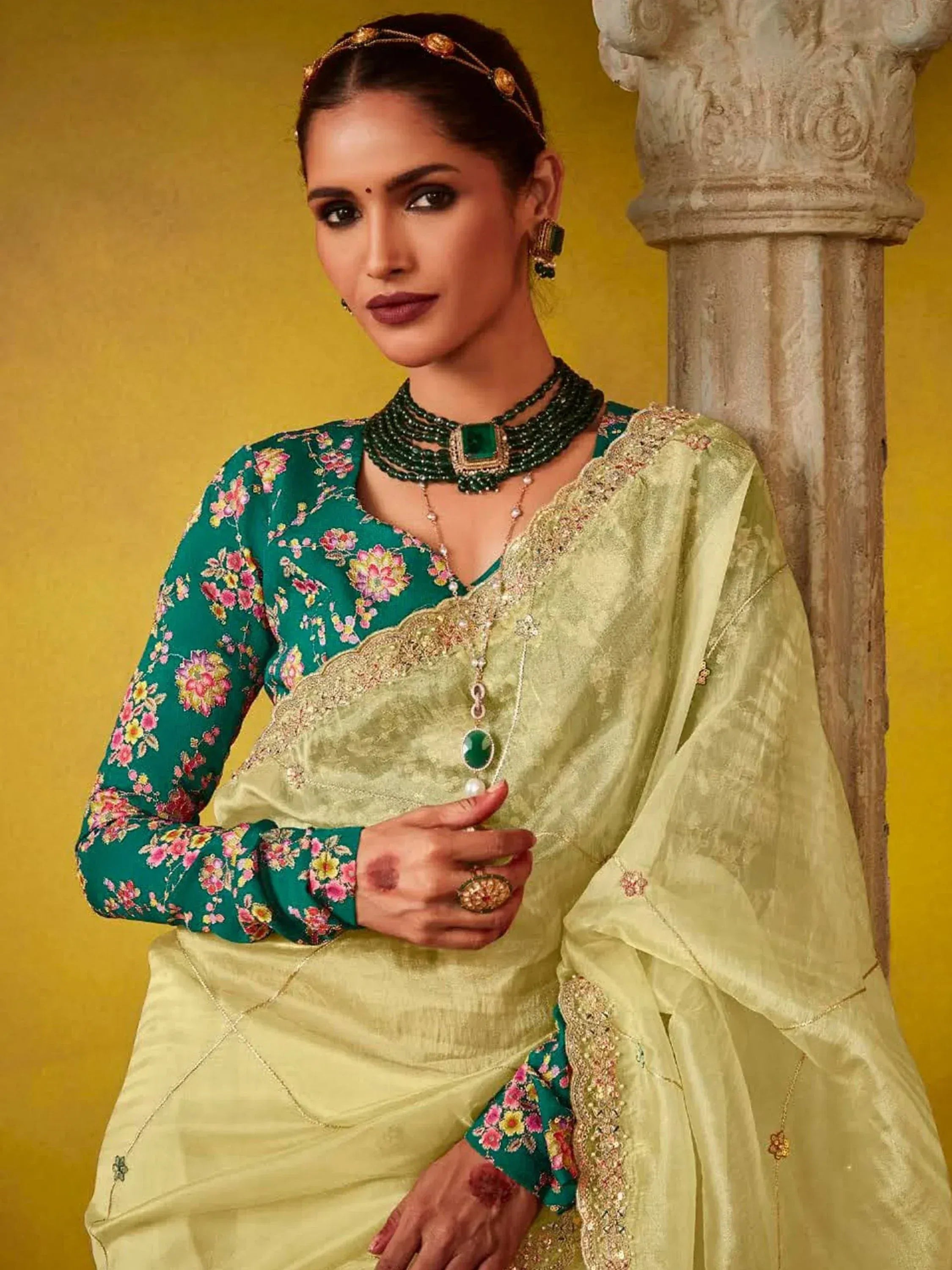 Woman in green floral blouse with light green saree, traditional Indian ethnic wear, adorned with emerald jewelry