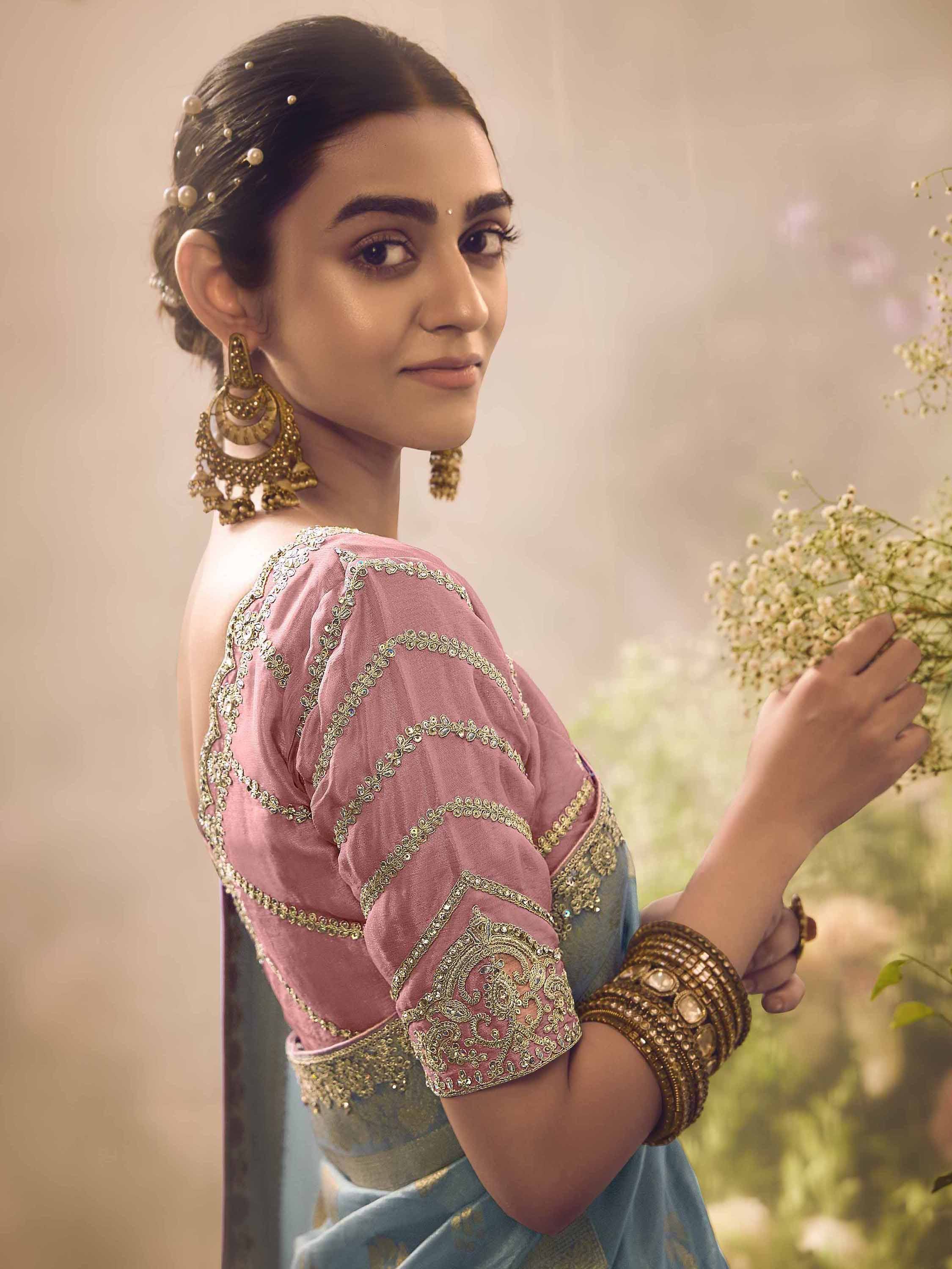 Woman in pink embroidered blouse with gold jewelry, holding flowers, styled for Indian ethnic wear