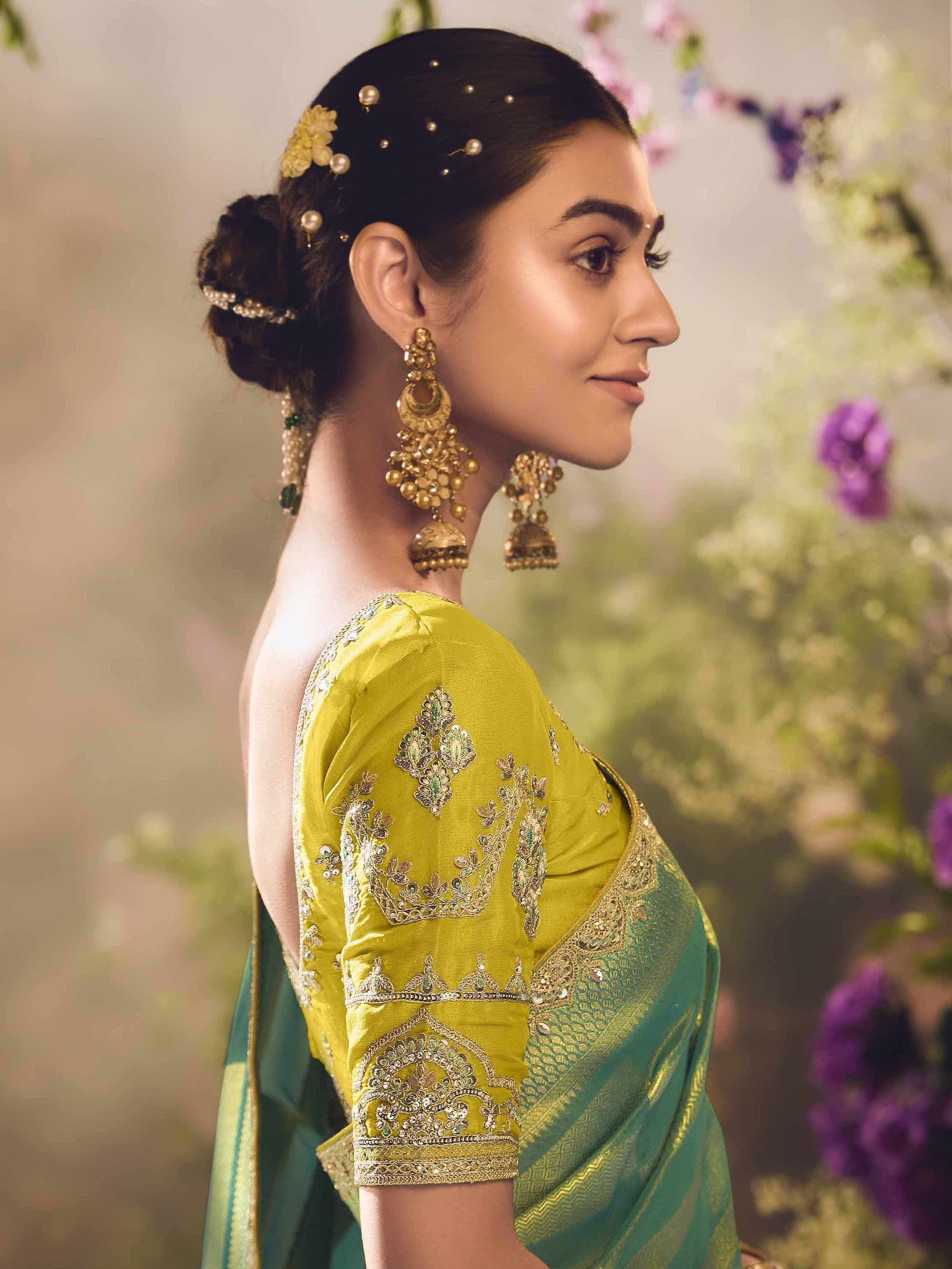 Woman in green and yellow embroidered saree with gold jewelry, floral backdrop