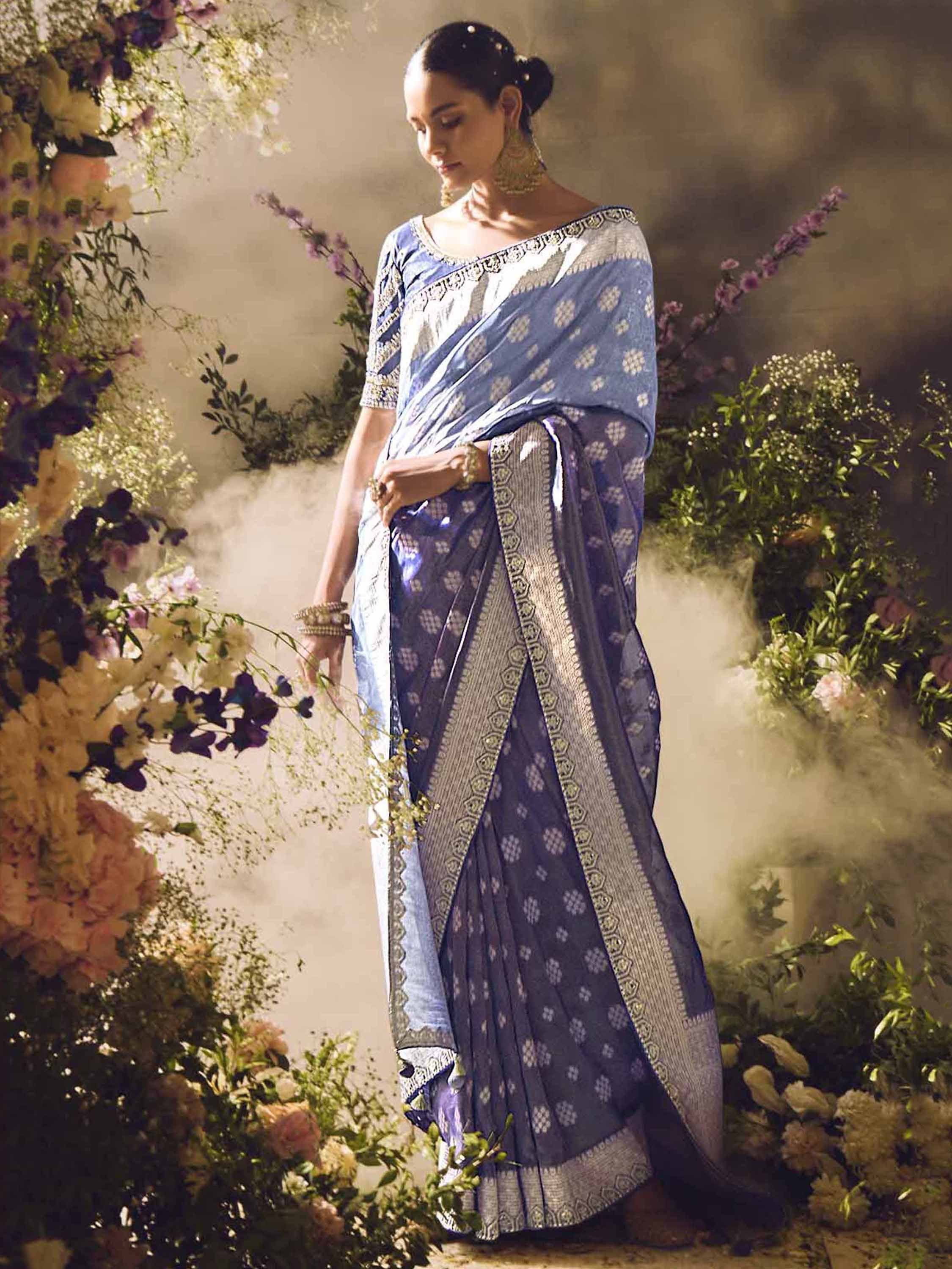 Blue floral printed saree with gold border, styled with ethnic jewelry amidst floral decor