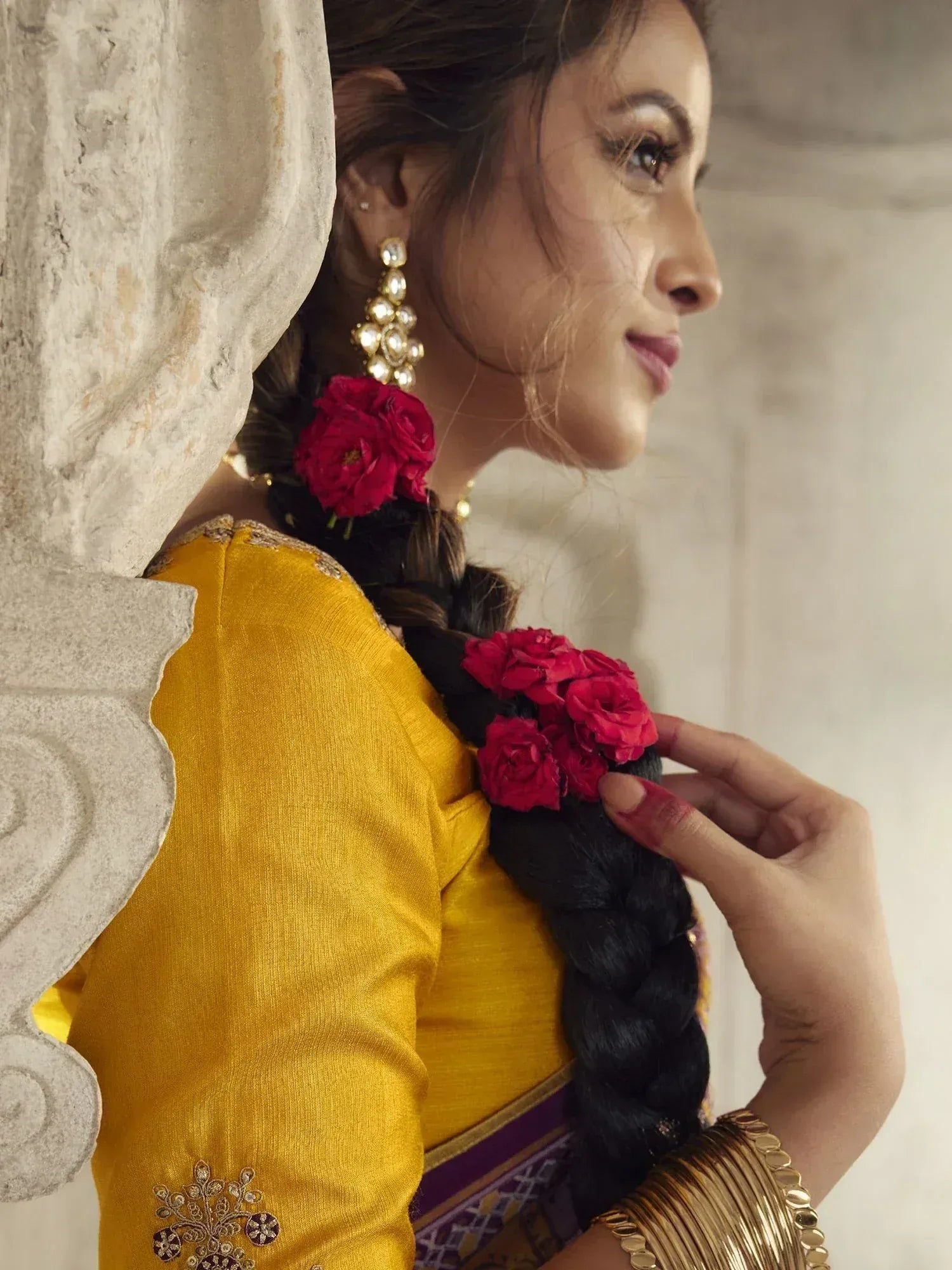 Woman in yellow ethnic wear with floral braid, gold jewelry, and traditional Indian styling