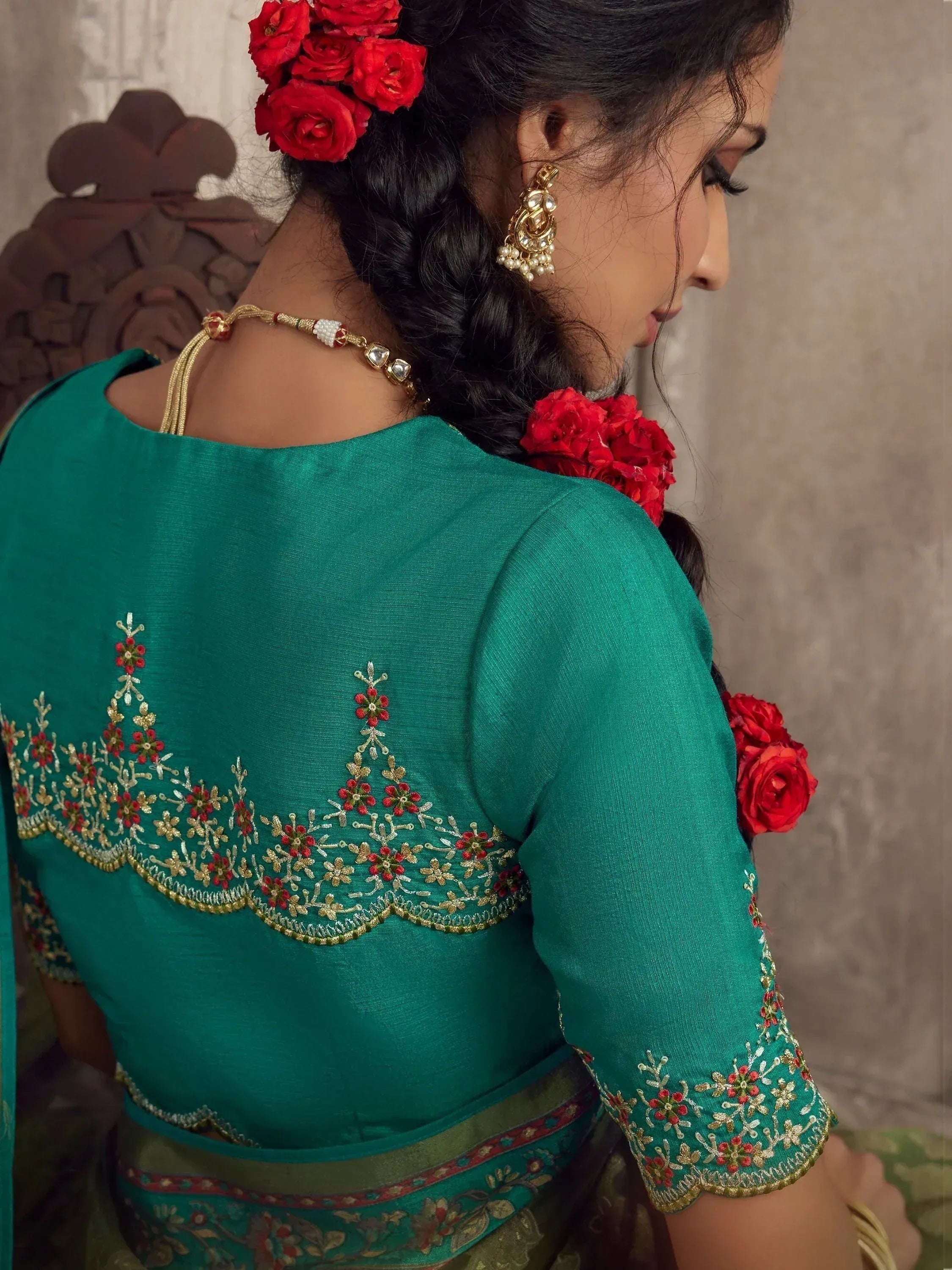 Emerald green ethnic blouse with gold and red floral embroidery, paired with traditional jewelry and rose hair accessories.