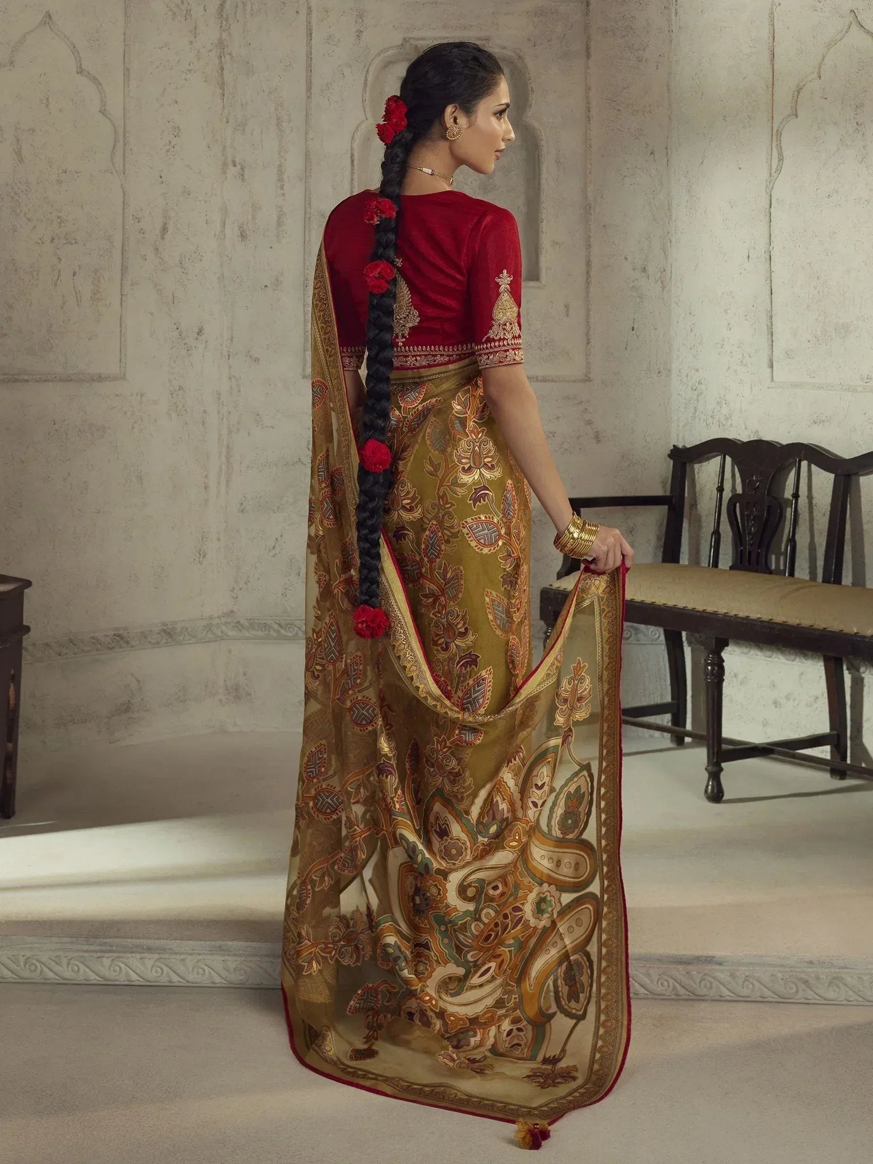 Woman in elegant Indian saree with gold paisley print, red blouse, and floral braid, showcasing traditional ethnic wear.