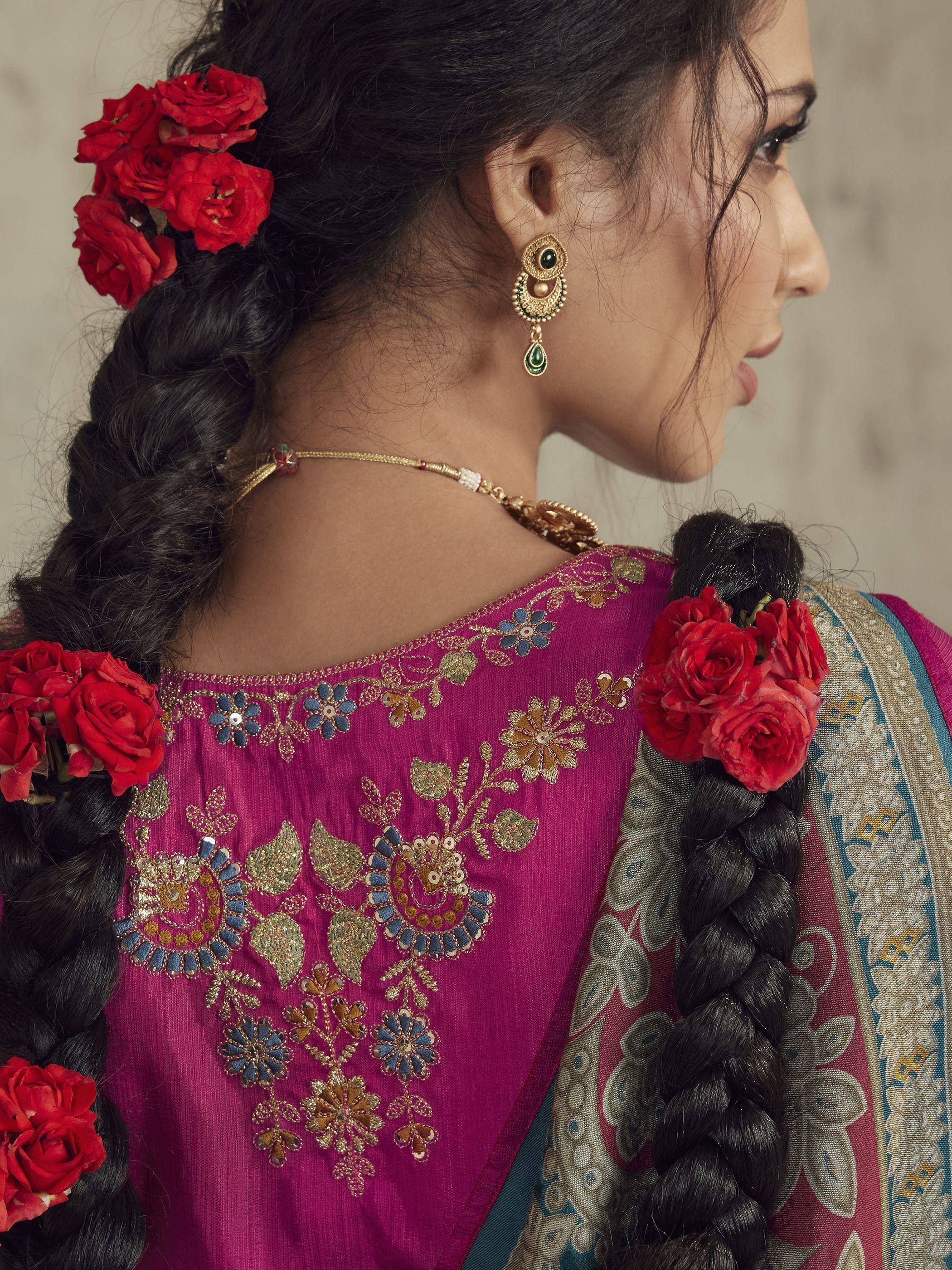 Woman in purple embroidered saree with floral hair accessories and gold jewelry, showcasing ethnic Indian fashion.