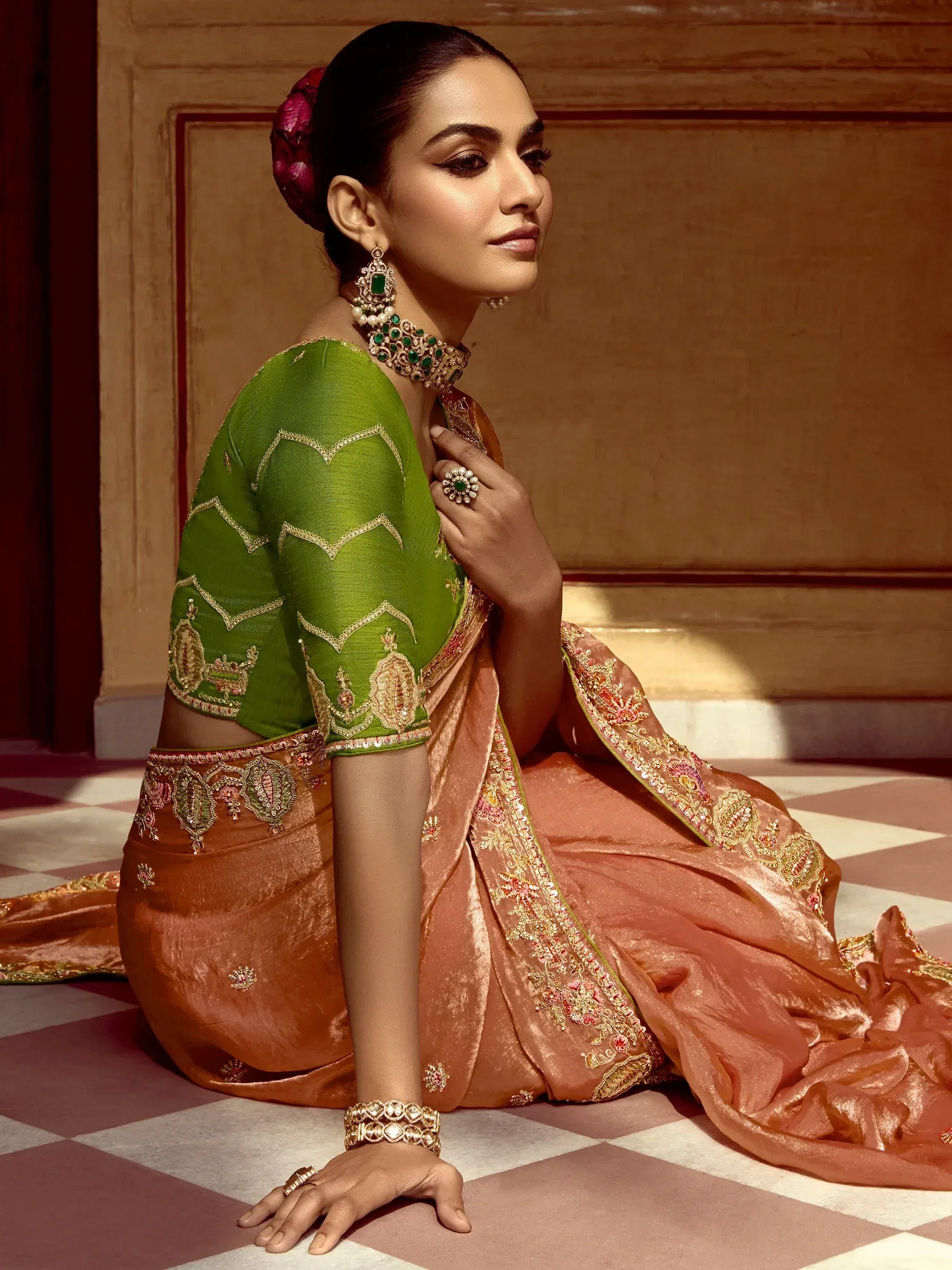 Elegant woman in green and peach designer saree with gold embroidery and emerald jewelry