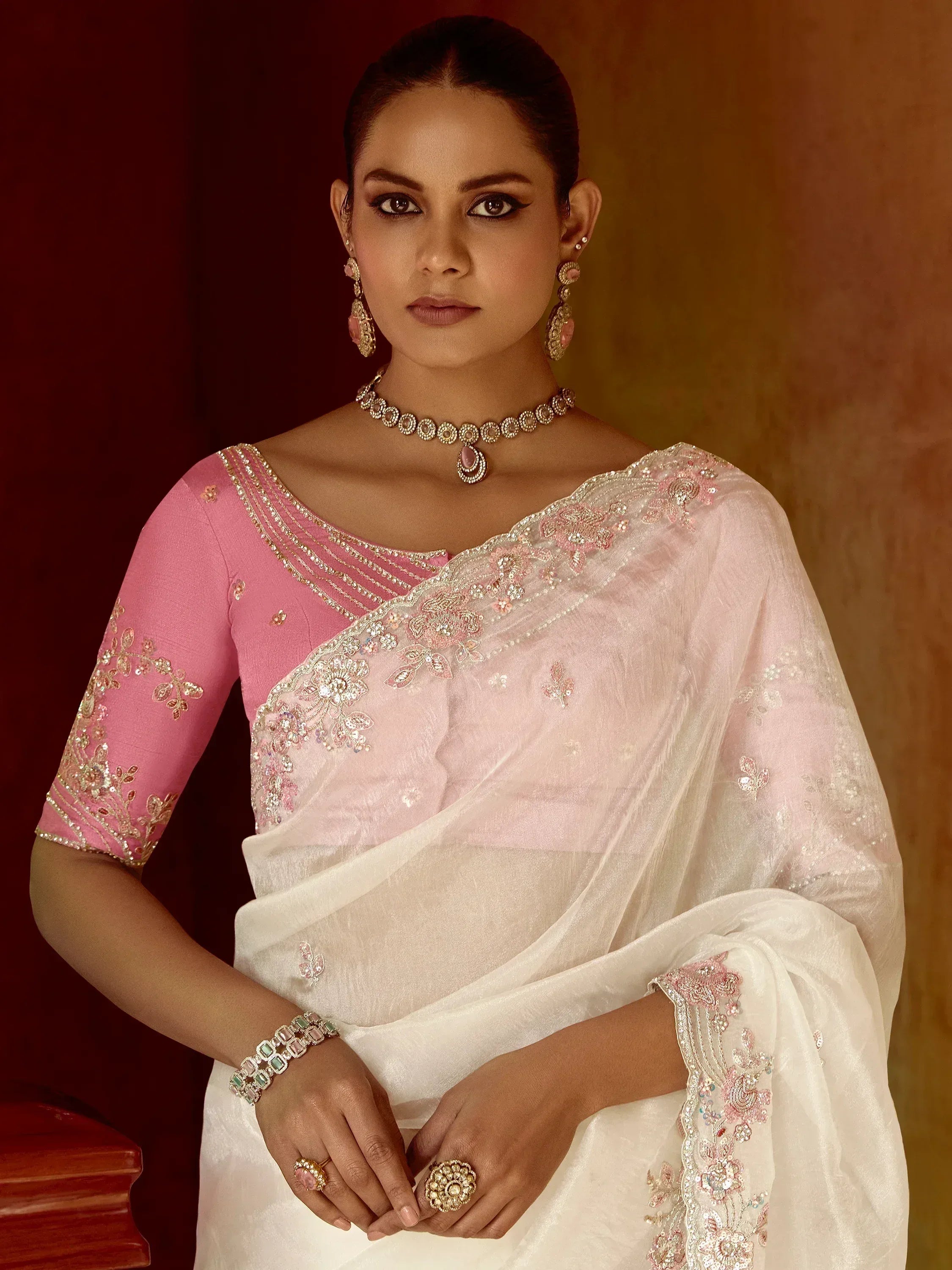 Elegant white saree with pink floral embroidery and matching blouse, accessorized with traditional jewelry