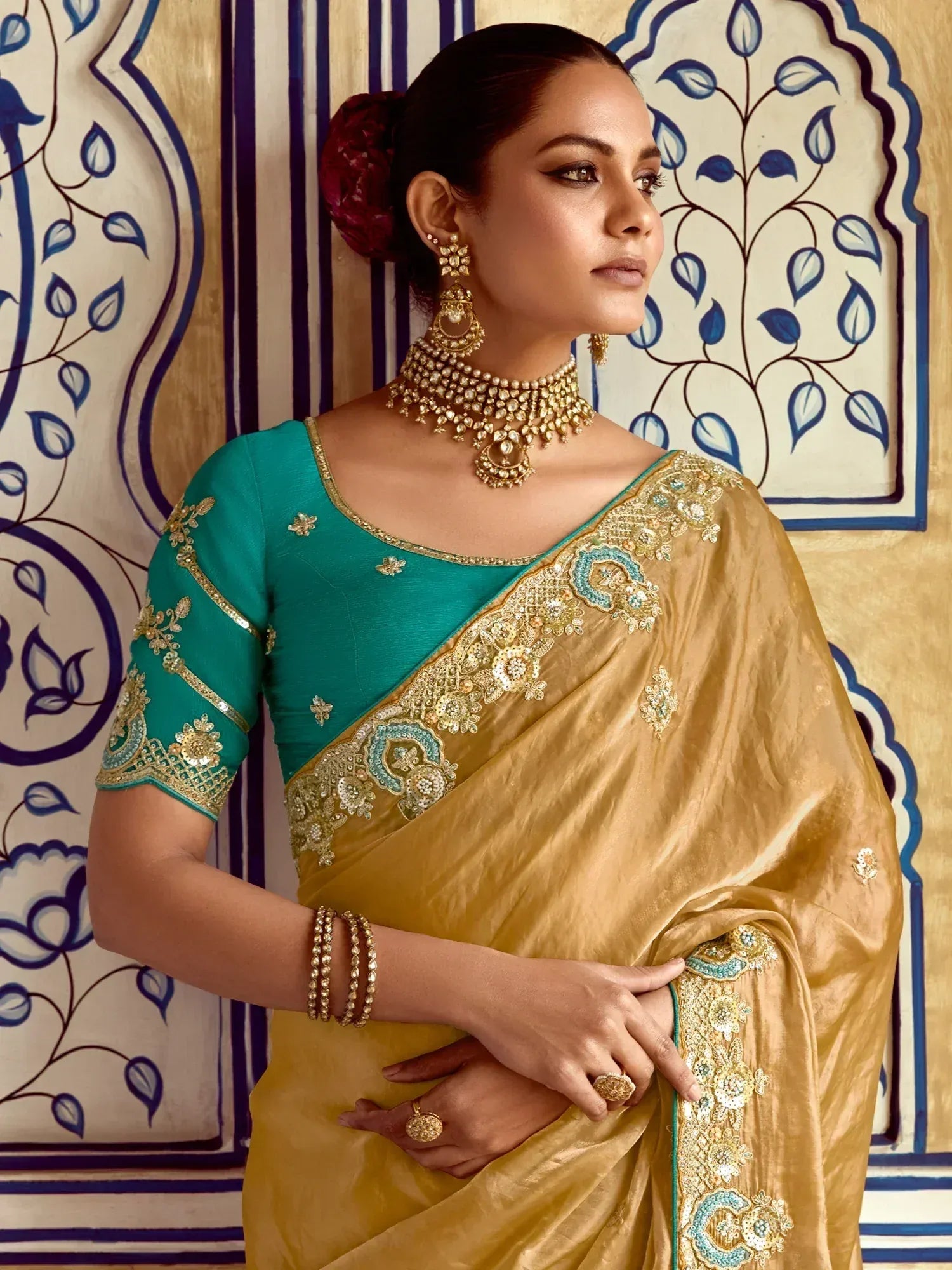 Elegant gold saree with teal blouse, intricate embroidery, and traditional jewelry for Indian ethnic wear.