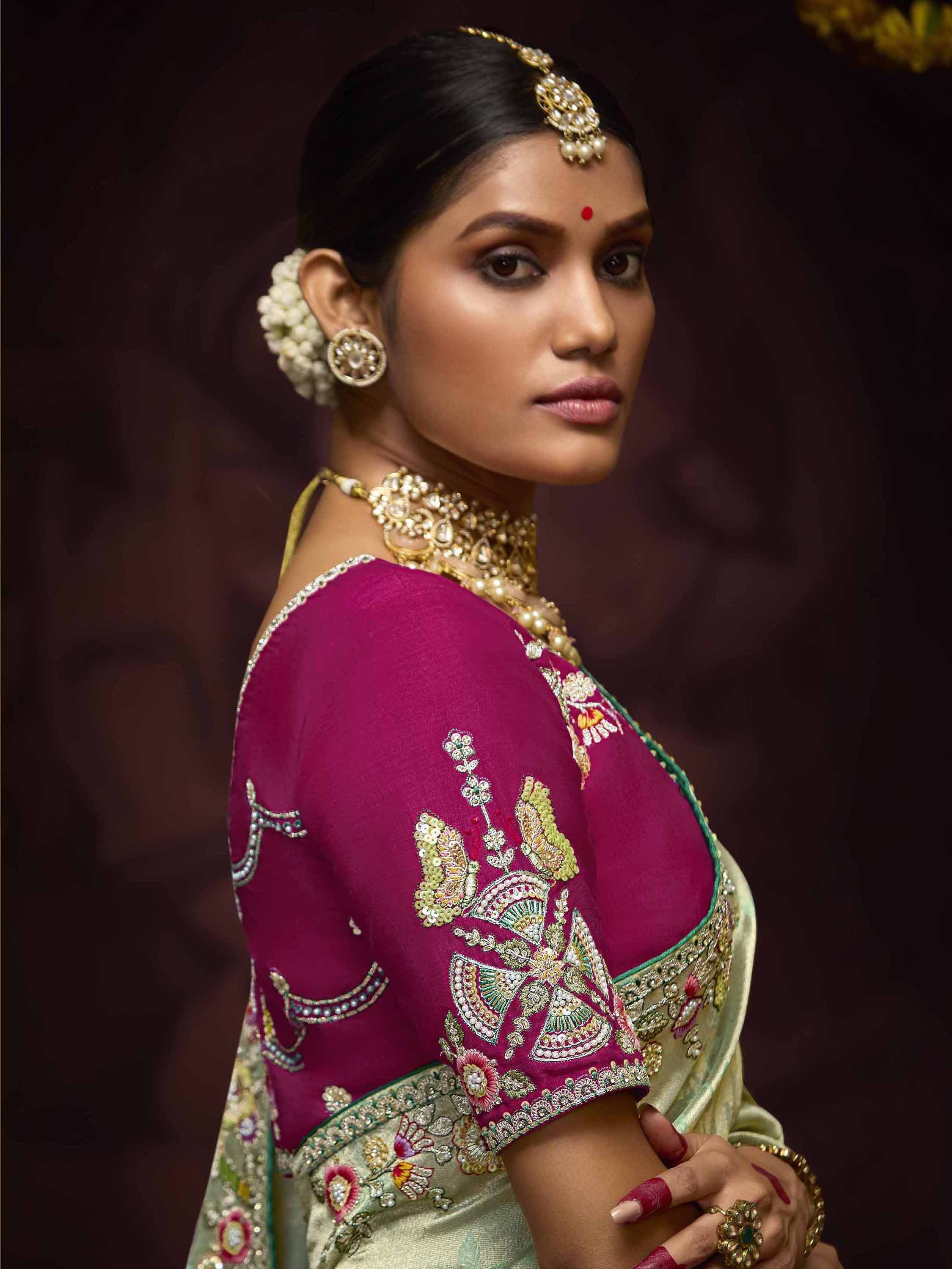 Woman in embroidered magenta blouse with gold jewelry, floral hair accessory, and traditional Indian saree