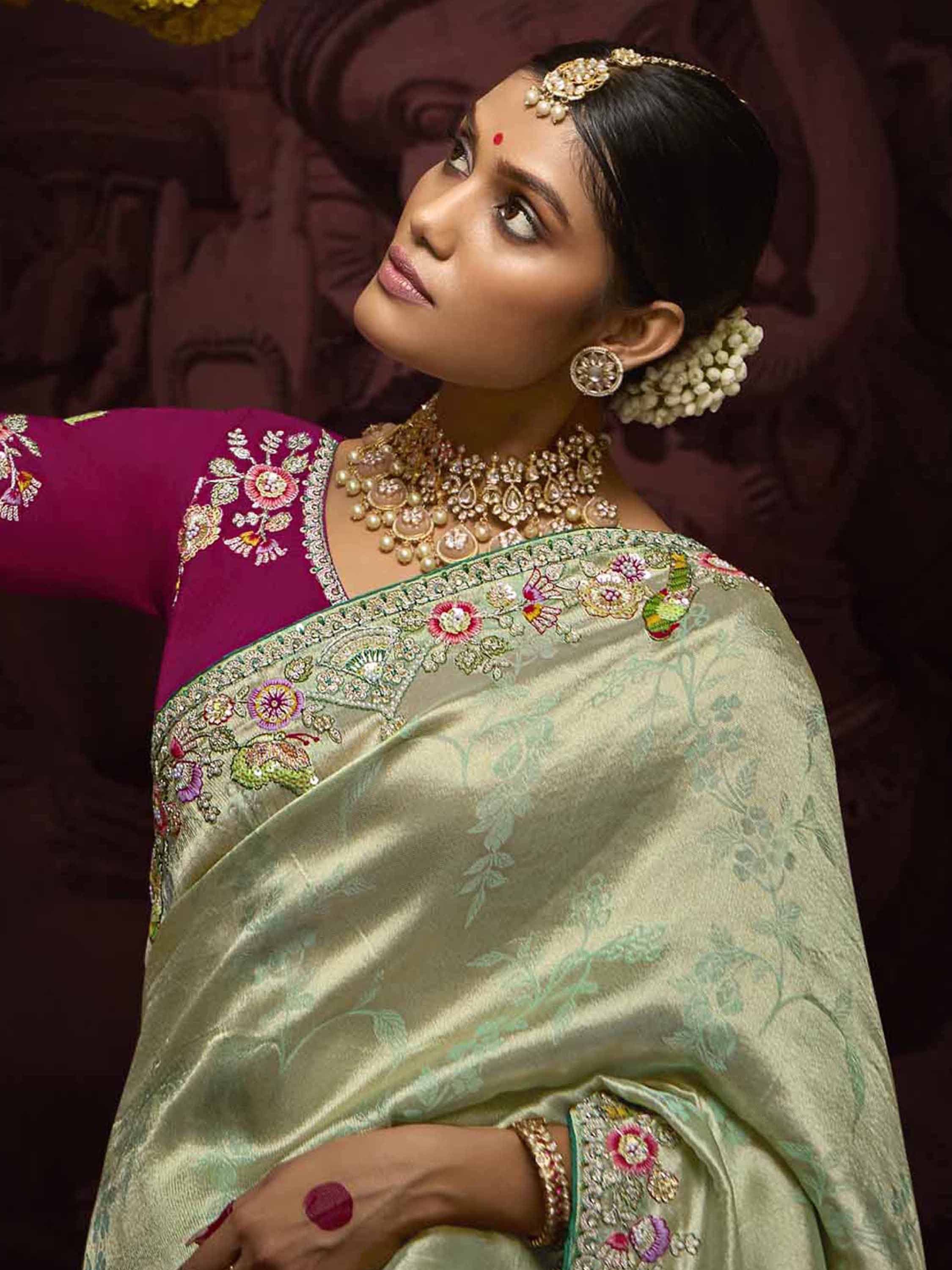 Elegant woman in embroidered green saree with purple blouse, traditional Indian jewelry, and floral hair accessory.