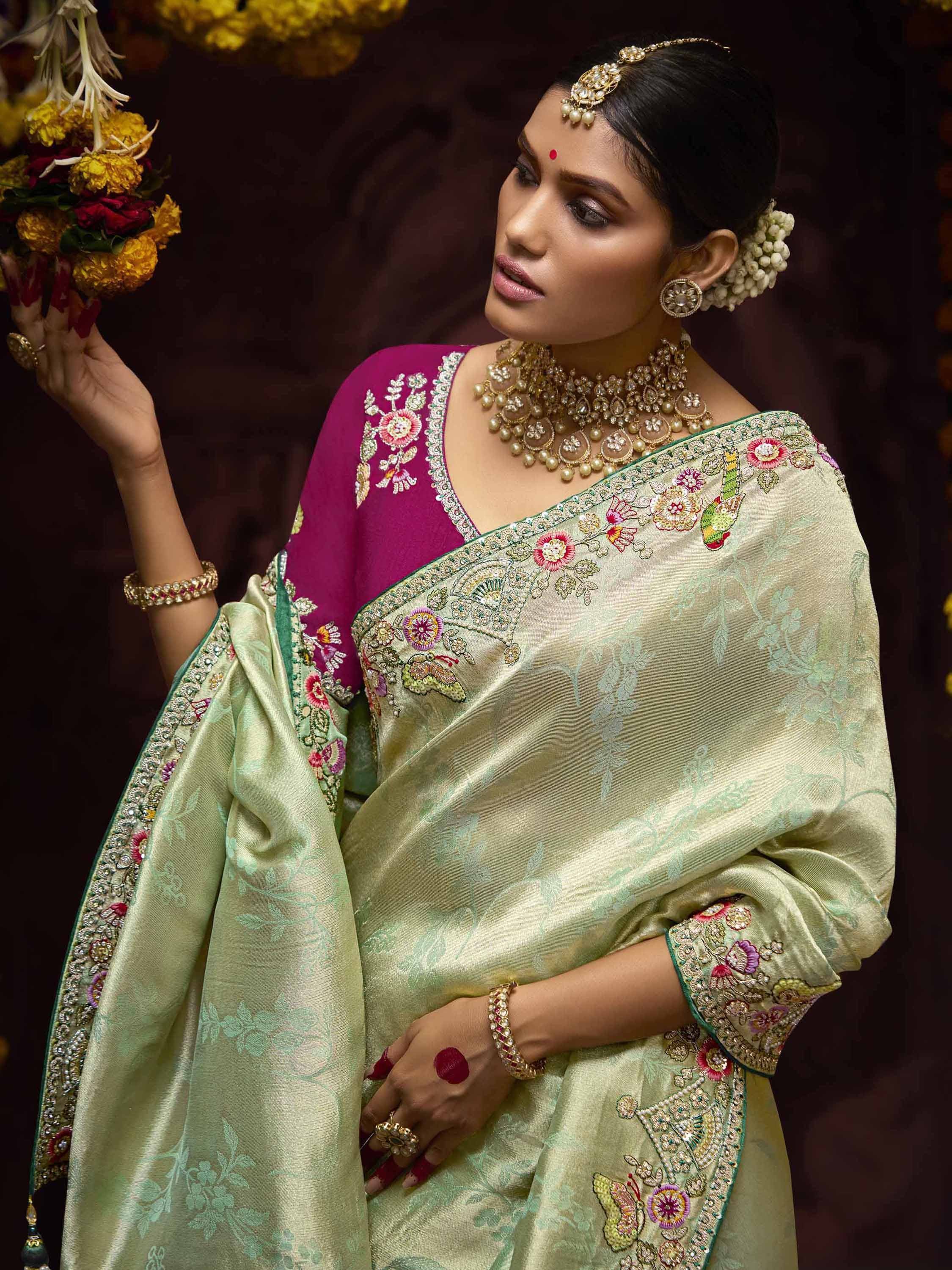 Elegant woman in embroidered green saree with pink blouse, gold jewelry, and floral garland, showcasing Indian ethnic wear.