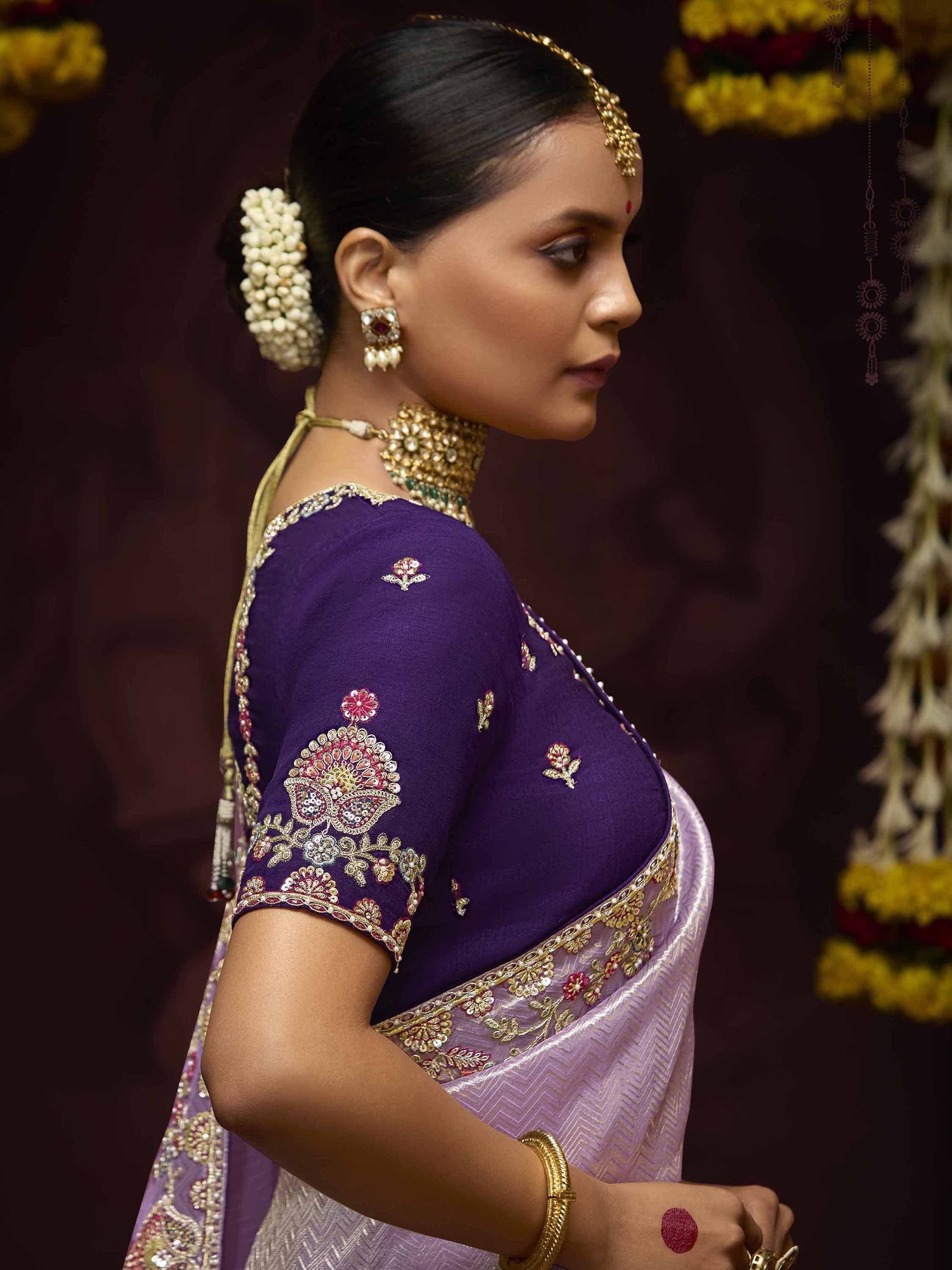 Woman in purple embroidered saree with gold jewelry and floral hair accessory, traditional Indian ethnic wear