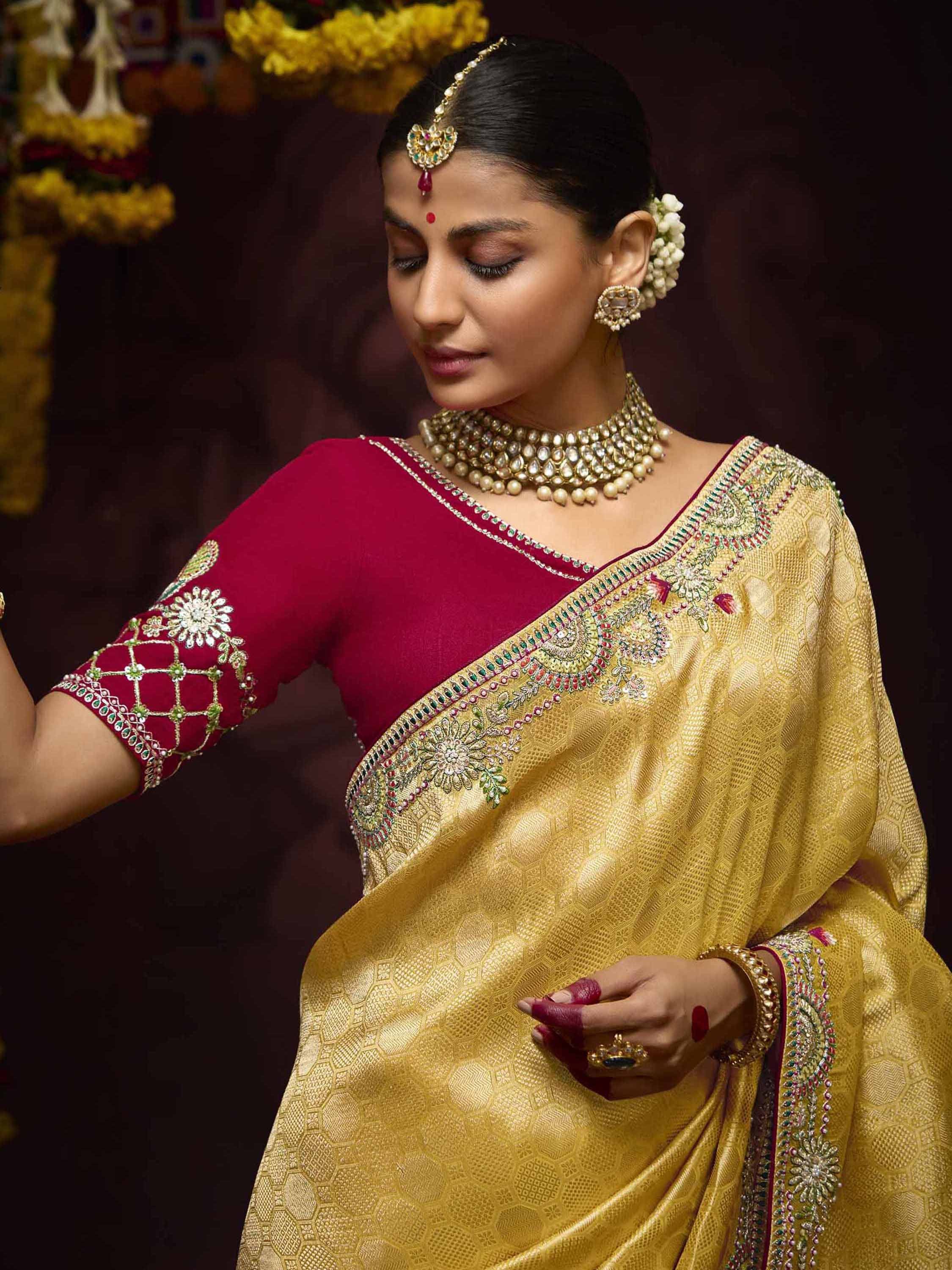 Elegant woman in gold embroidered saree with maroon blouse, traditional jewelry, and floral hair accessory