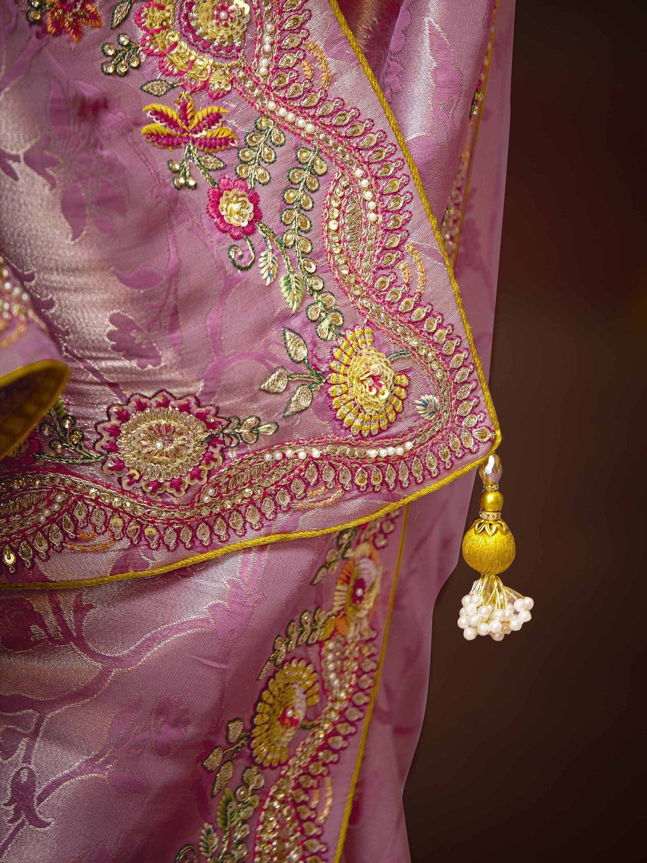 Pink ethnic saree with gold floral embroidery, pearl detailing, and tassel border