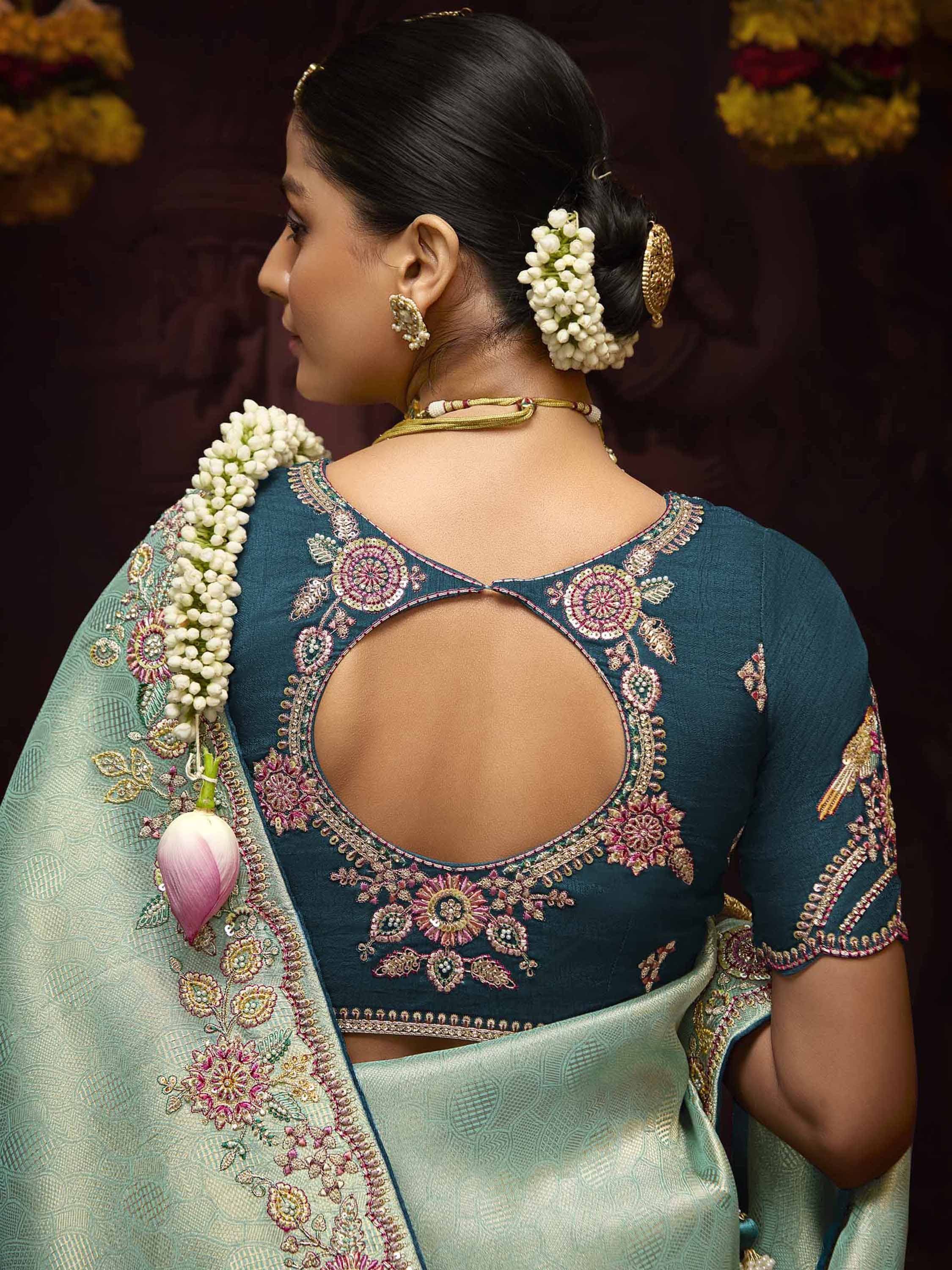 Teal embroidered blouse with back cutout, paired with mint saree, floral hair accessories, and gold jewelry