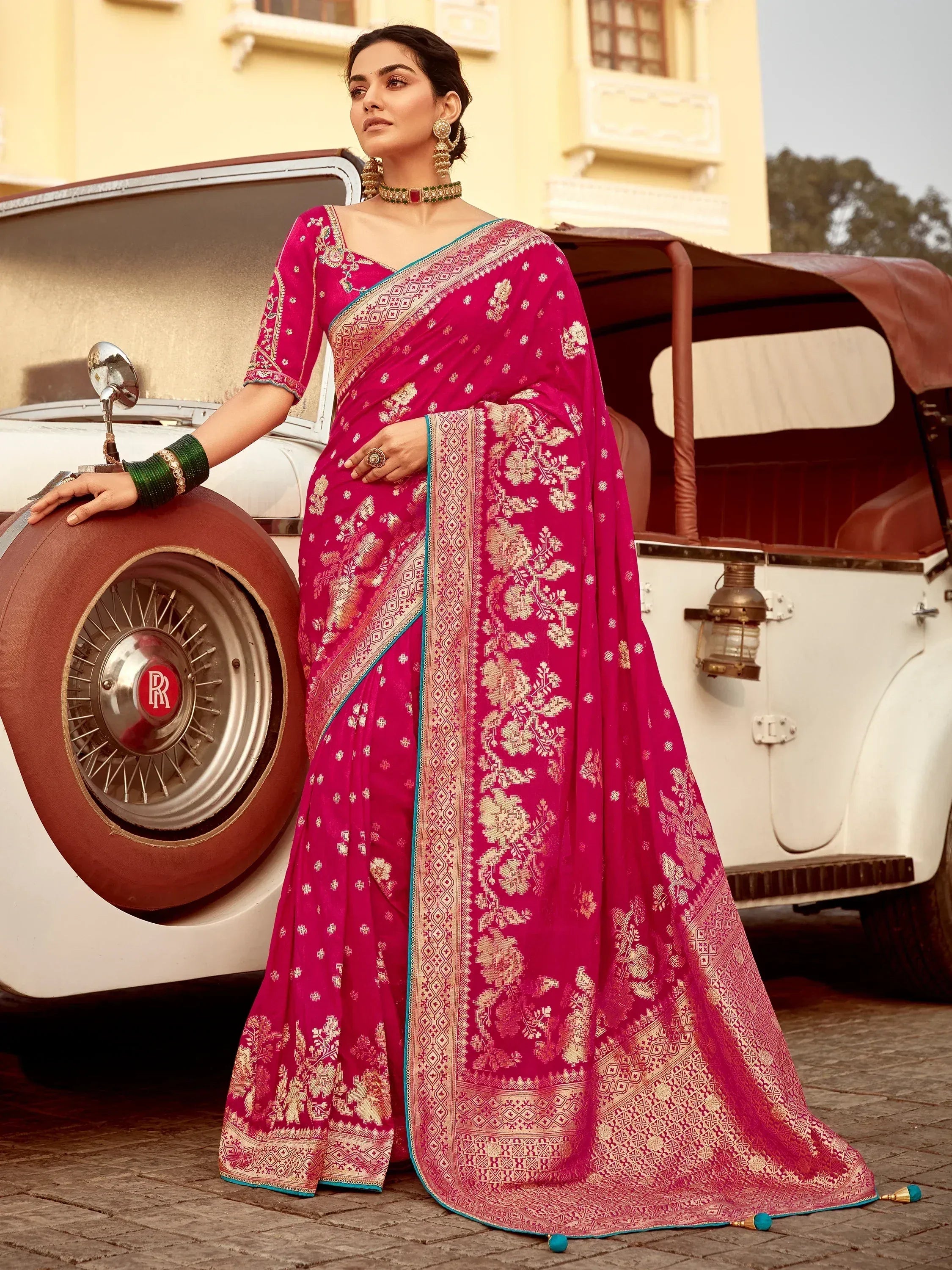 Elegant pink saree with gold floral embroidery, paired with traditional jewelry, styled beside a vintage car.
