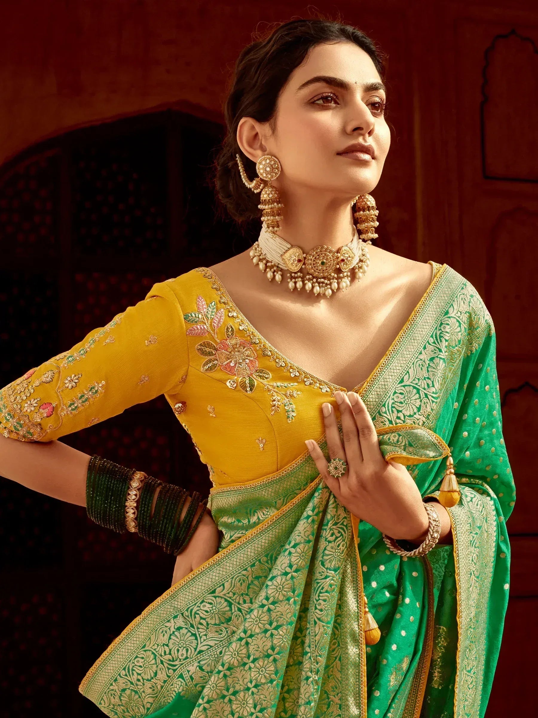 Elegant woman in yellow embroidered blouse and green floral saree with gold jewelry, showcasing Indian ethnic wear.