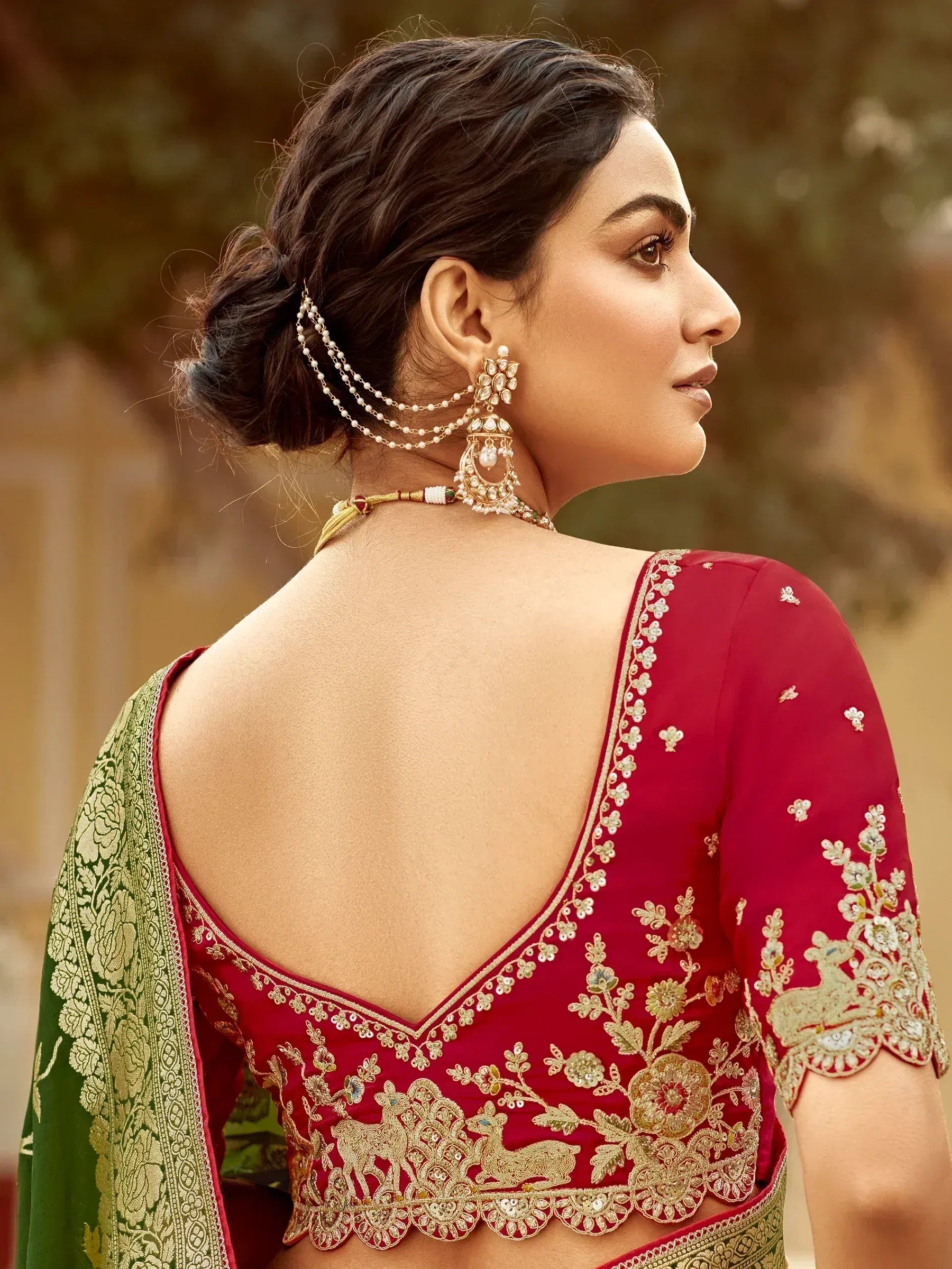 Red embroidered blouse with gold floral designs and green saree, paired with traditional jewelry