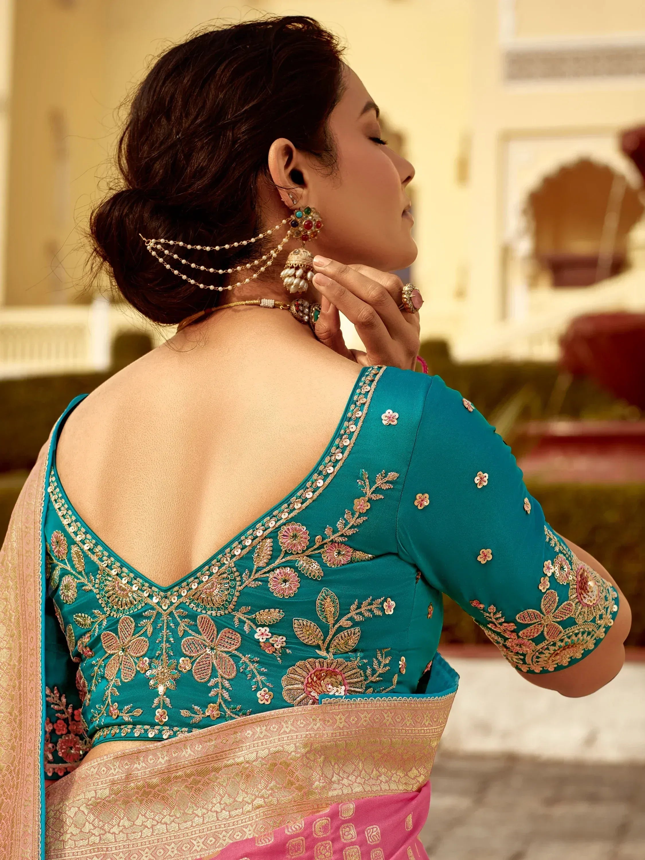 Teal embroidered saree blouse with floral designs and gold detailing, paired with traditional jewelry