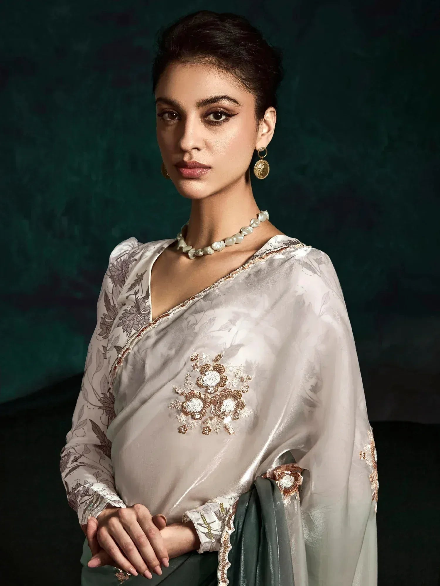 Elegant Indian saree with floral embroidery and gold detailing, paired with pearl necklace and statement earrings.