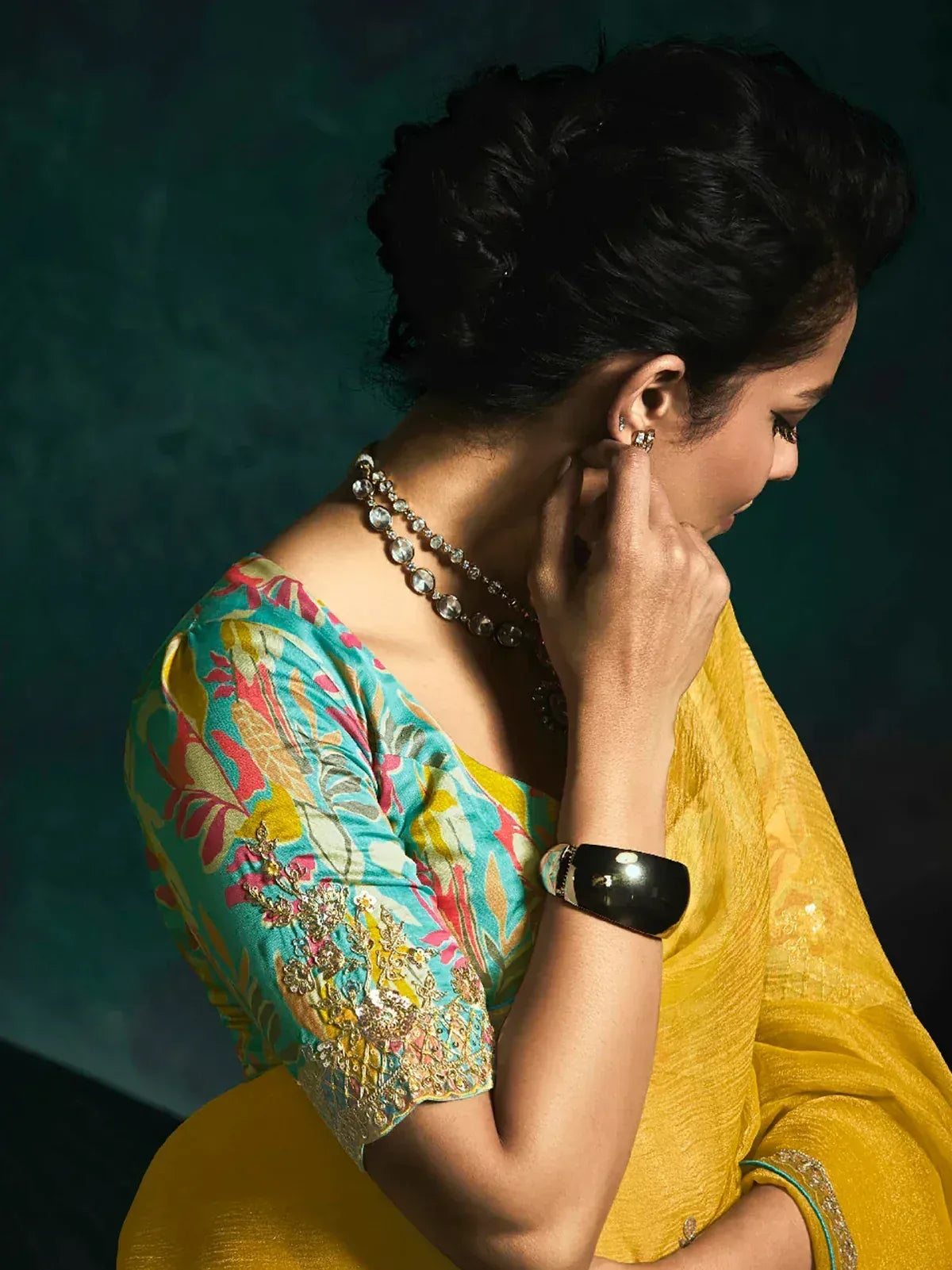 Woman in vibrant yellow saree with floral blouse, adjusting earrings, showcasing ethnic Indian fashion