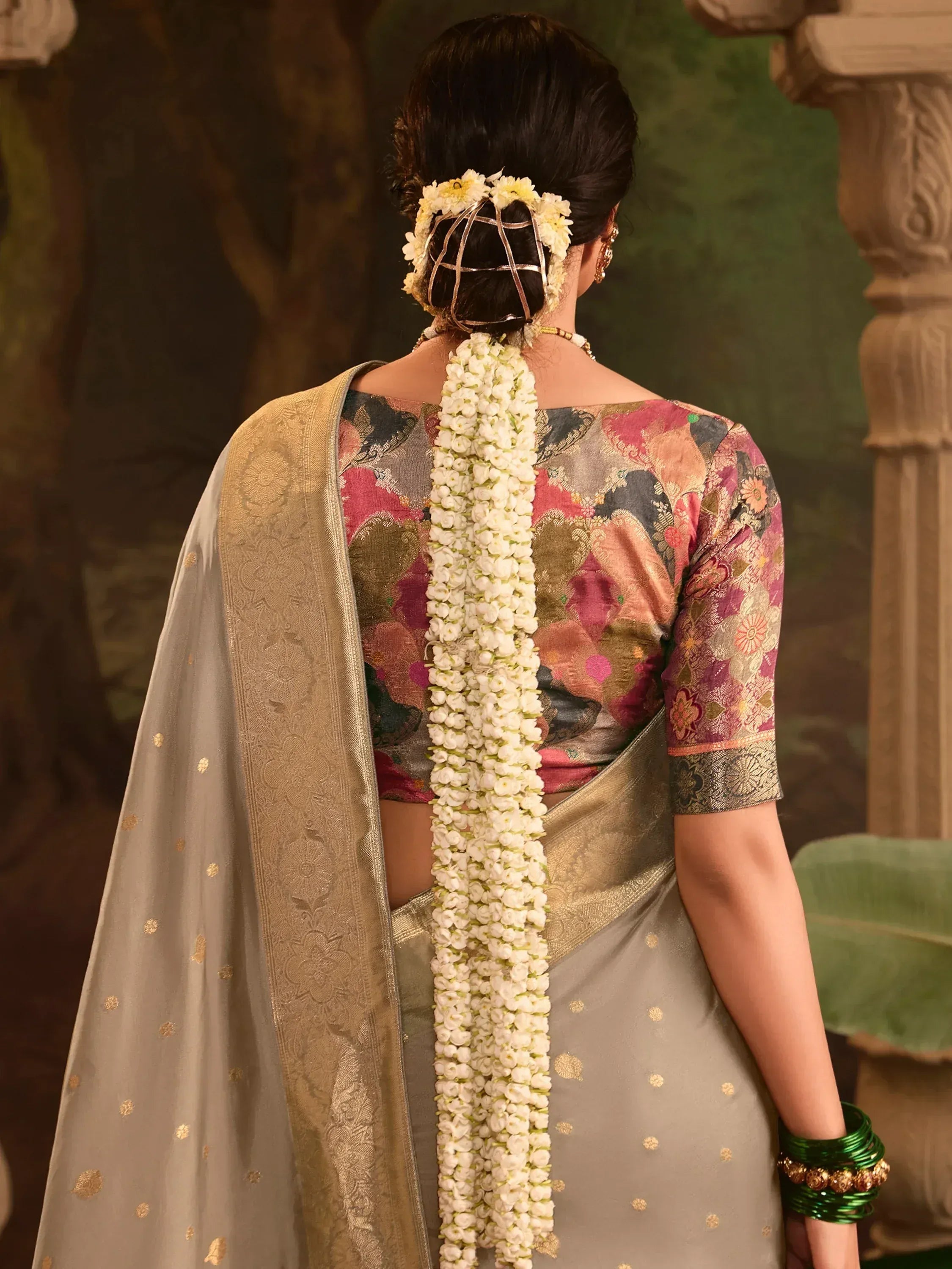 Woman in floral print saree with gold border, white flower gajra, and green bangles, back view