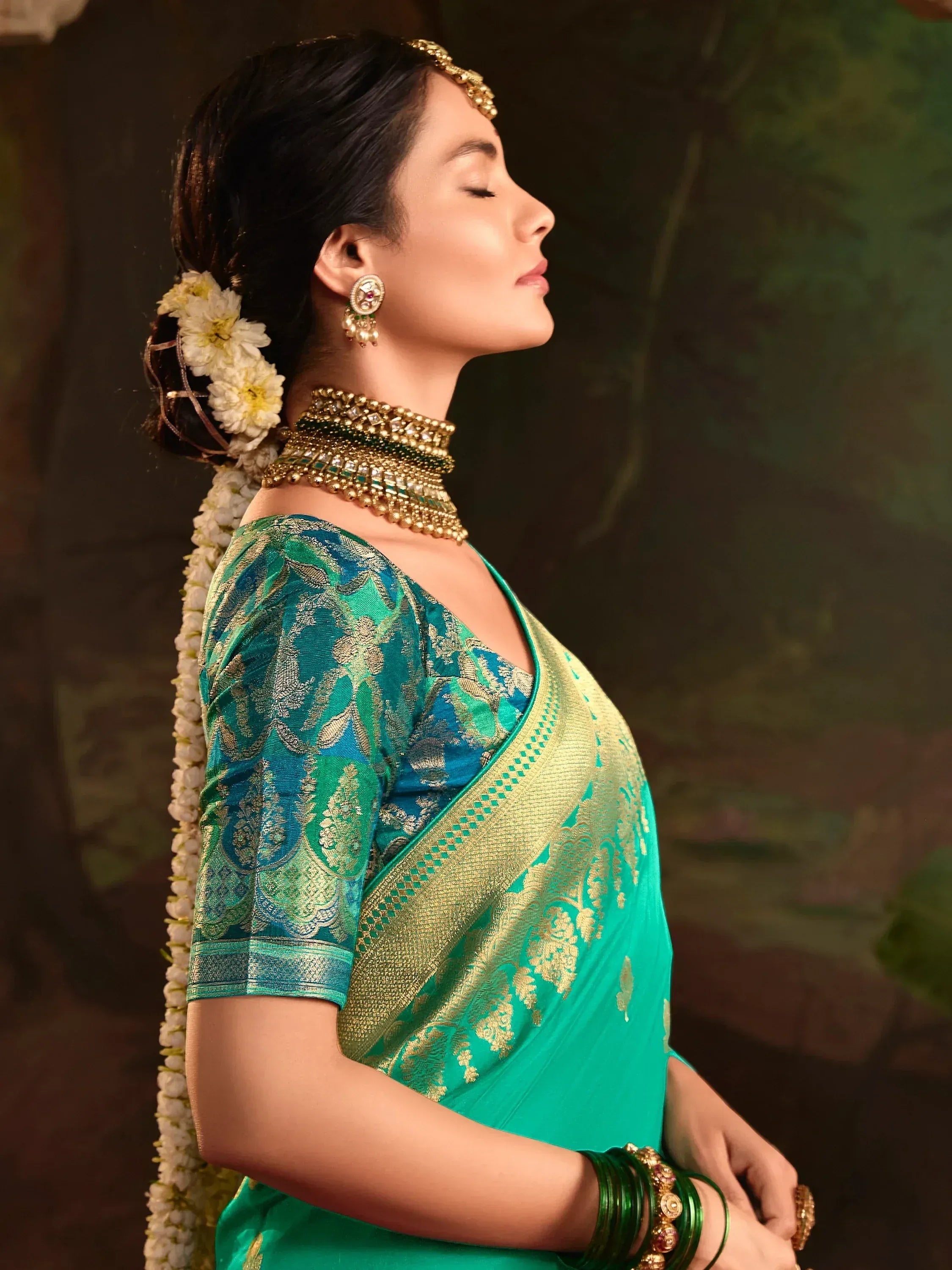 Elegant woman in teal designer saree with gold embroidery, floral hair accessory, and traditional jewelry