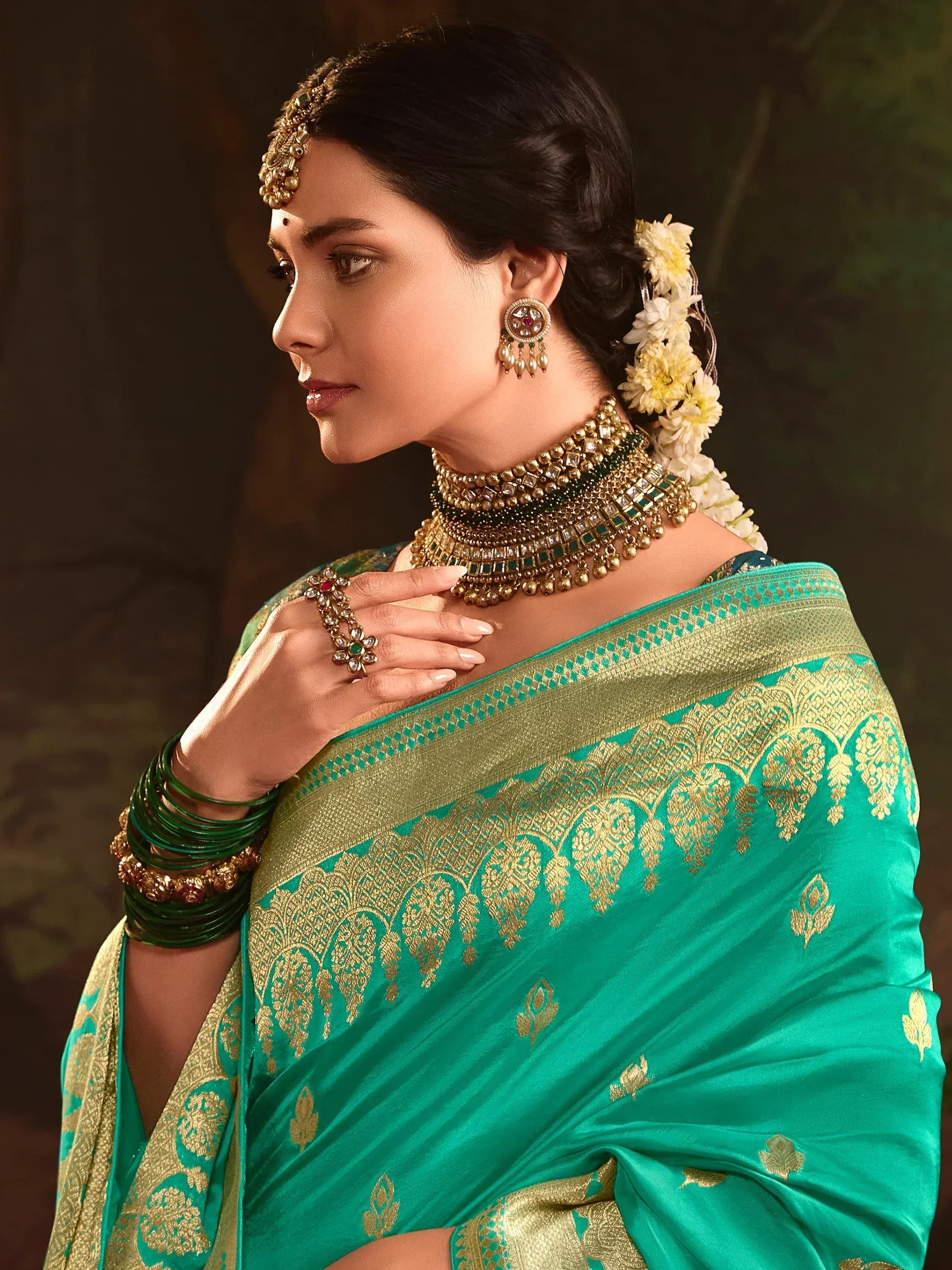 Elegant woman in green and gold embroidered saree with traditional Indian jewelry and floral hair adornment