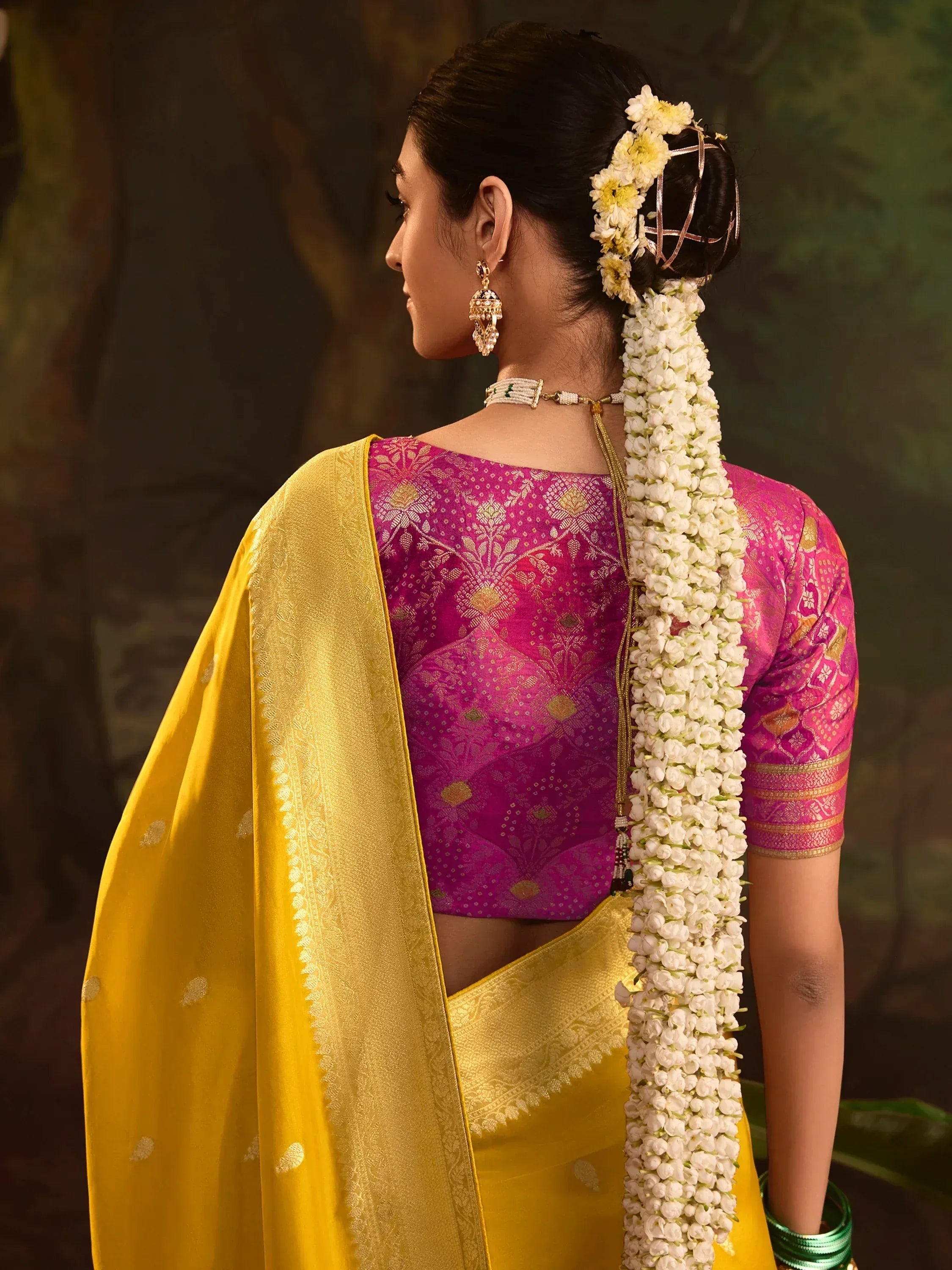 Woman in vibrant pink and gold saree with floral hair accessories, showcasing traditional Indian ethnic wear.