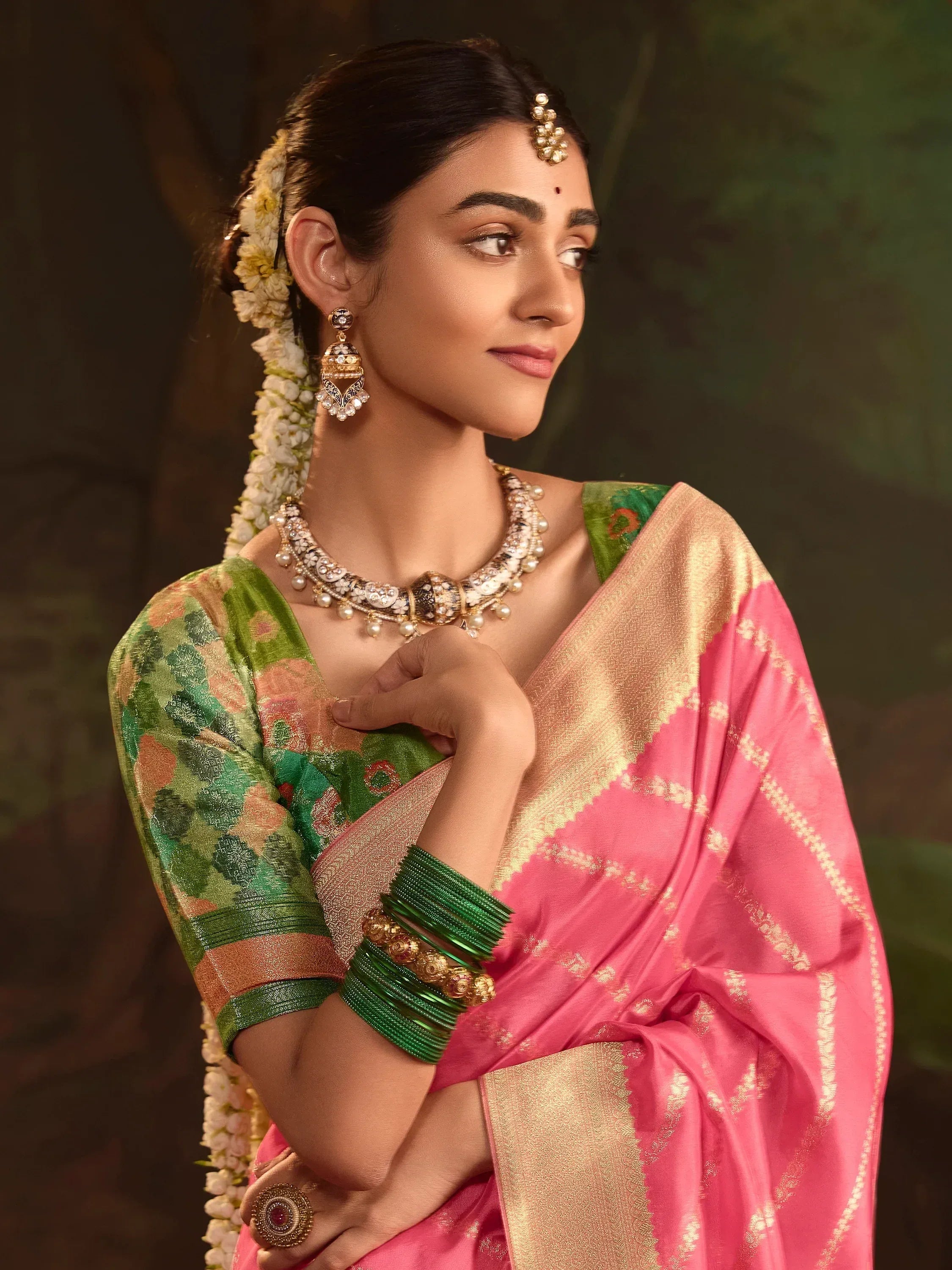 Woman in pink and green ethnic saree with gold jewelry and floral hair adornment