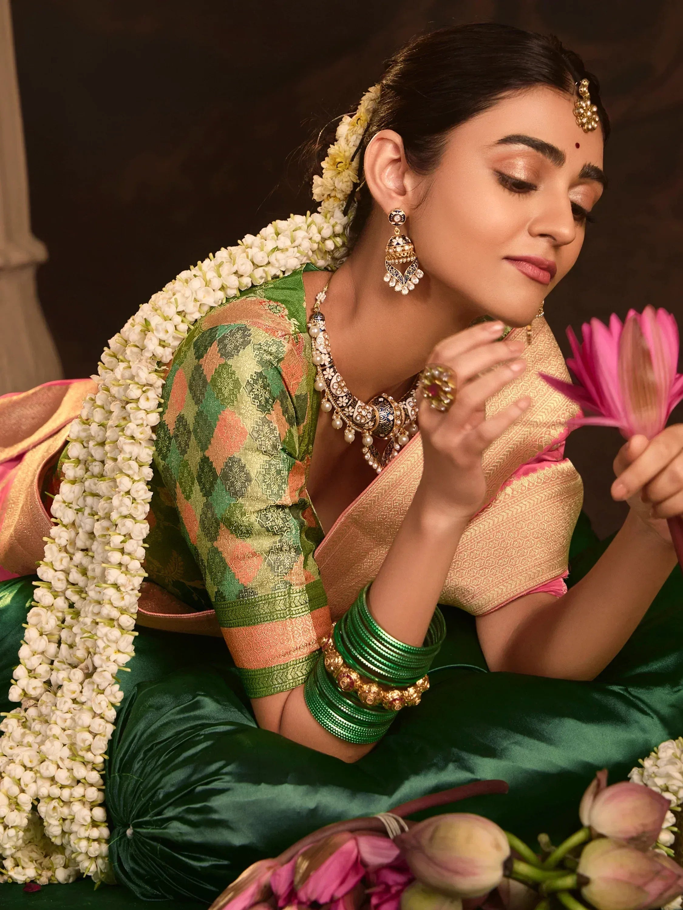 Woman in green and gold ethnic saree with floral garland, traditional jewelry, holding pink lotus