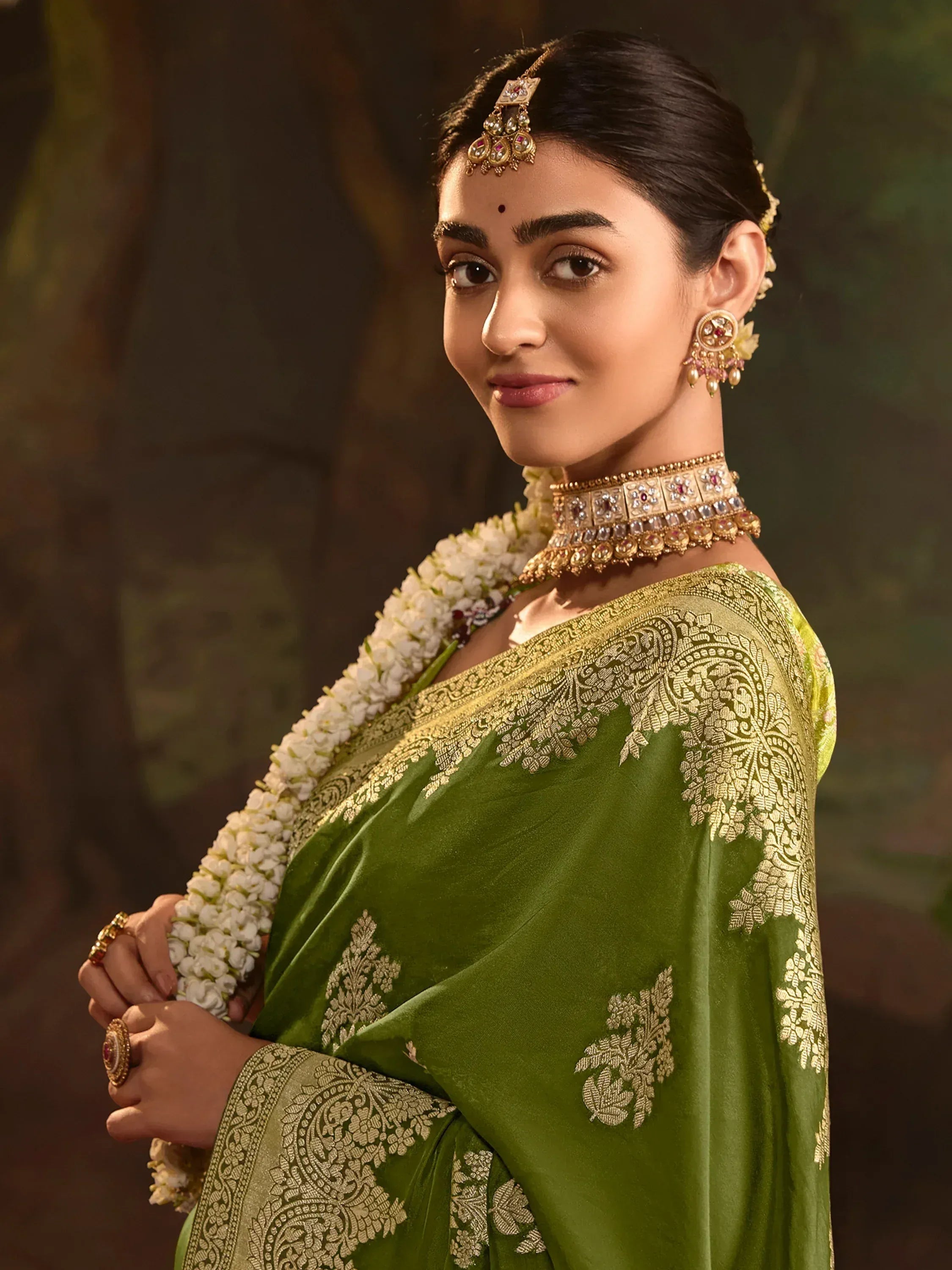Woman in green embroidered saree with gold jewelry and floral garland, traditional Indian ethnic wear