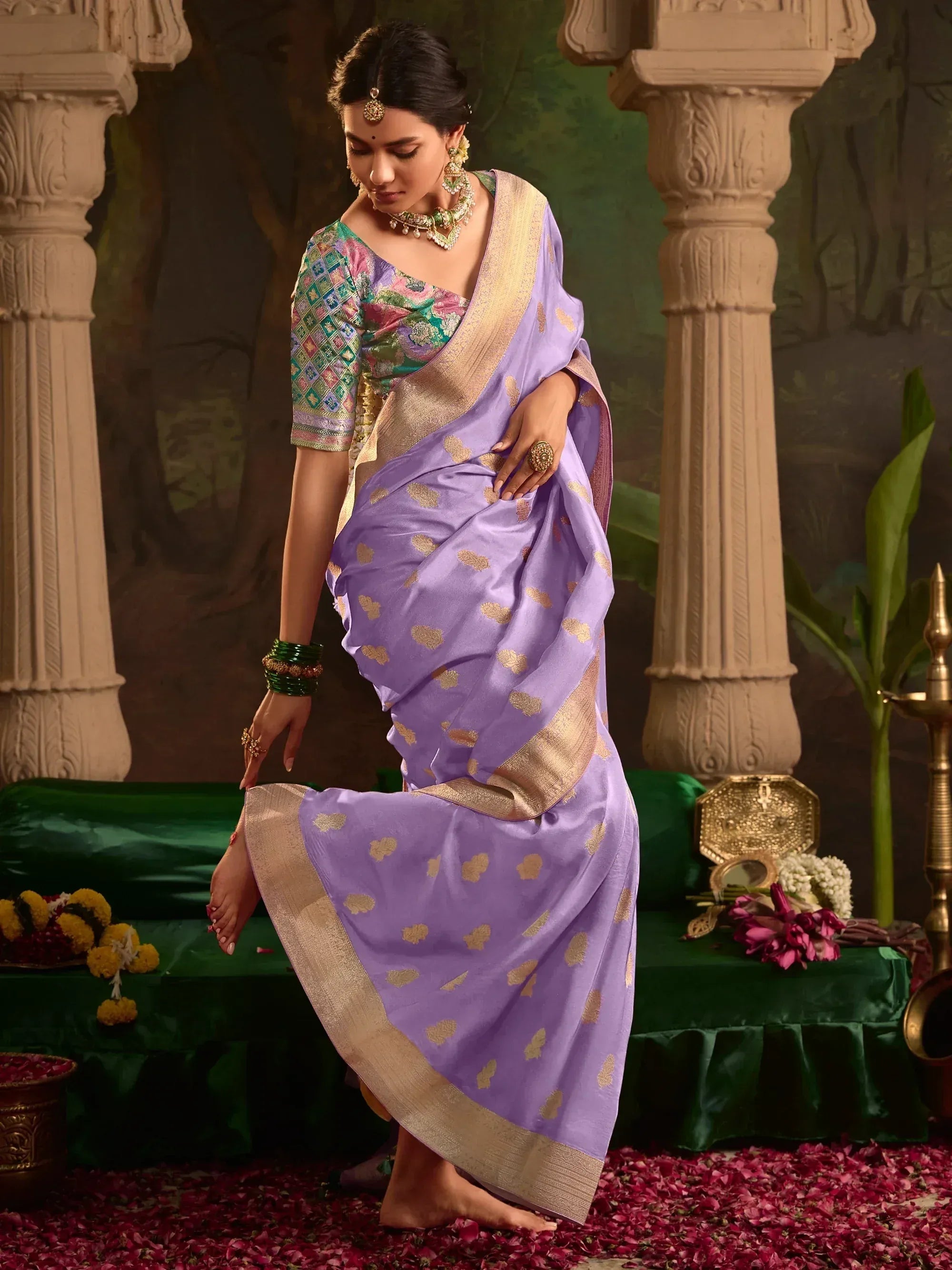 Woman in lavender saree with gold motifs, floral blouse, traditional jewelry, rose petals, temple pillars