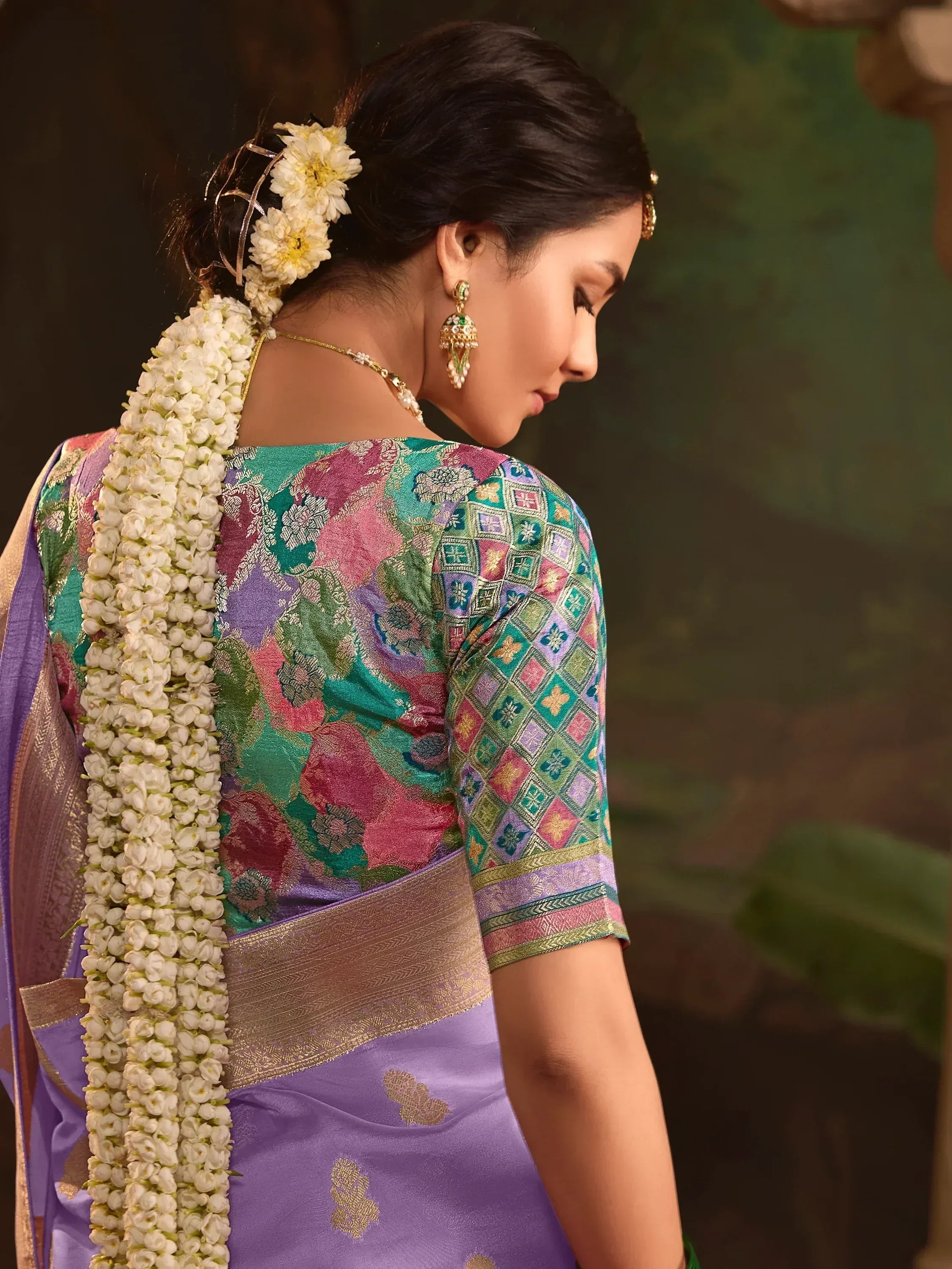 Woman in colorful floral saree with white flower garland and gold jewelry