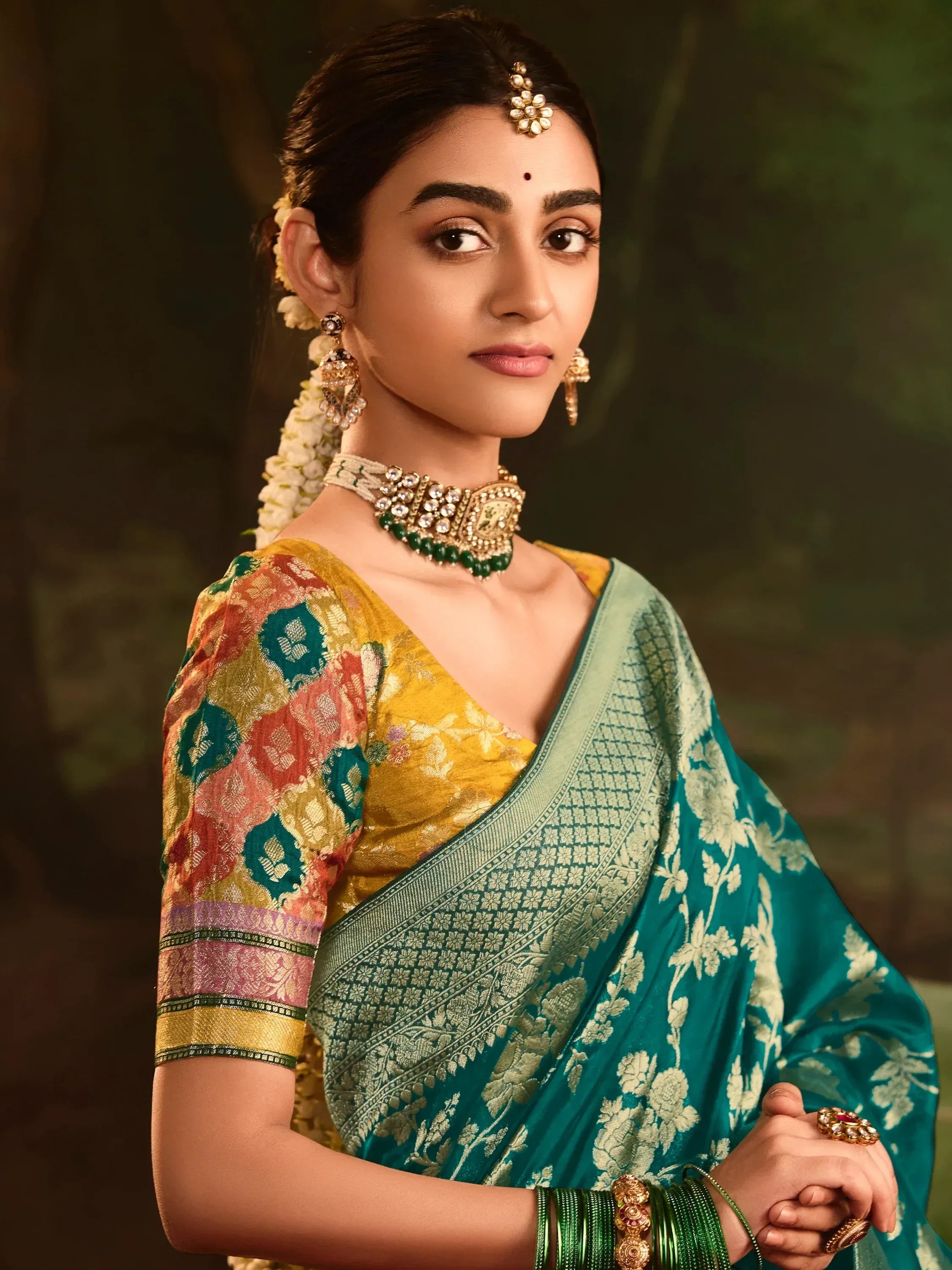 Woman in teal and gold floral saree with traditional jewelry, perfect for Indian ethnic wear occasions.