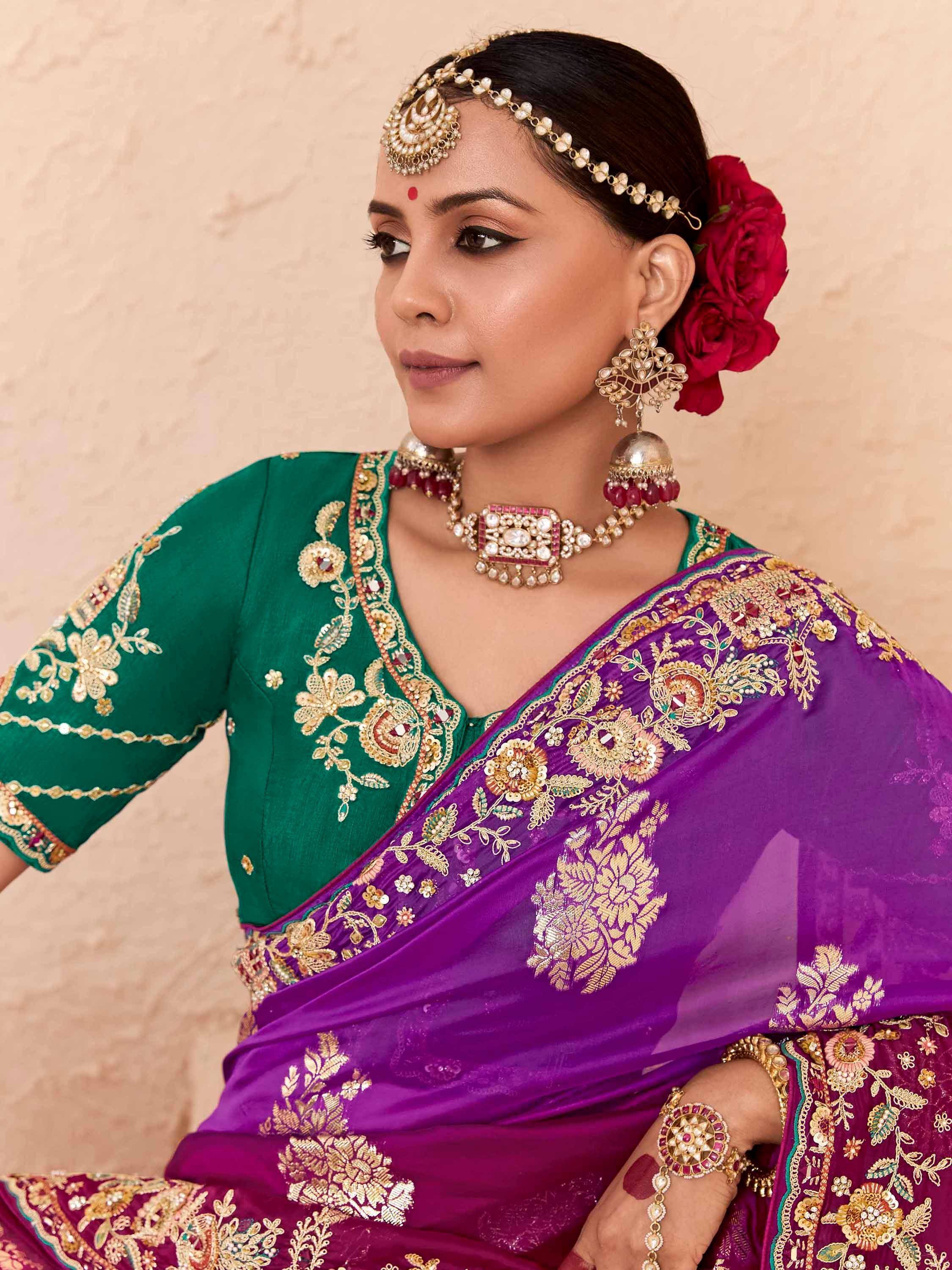 Woman in purple and green embroidered saree with gold jewelry and floral hair accessory