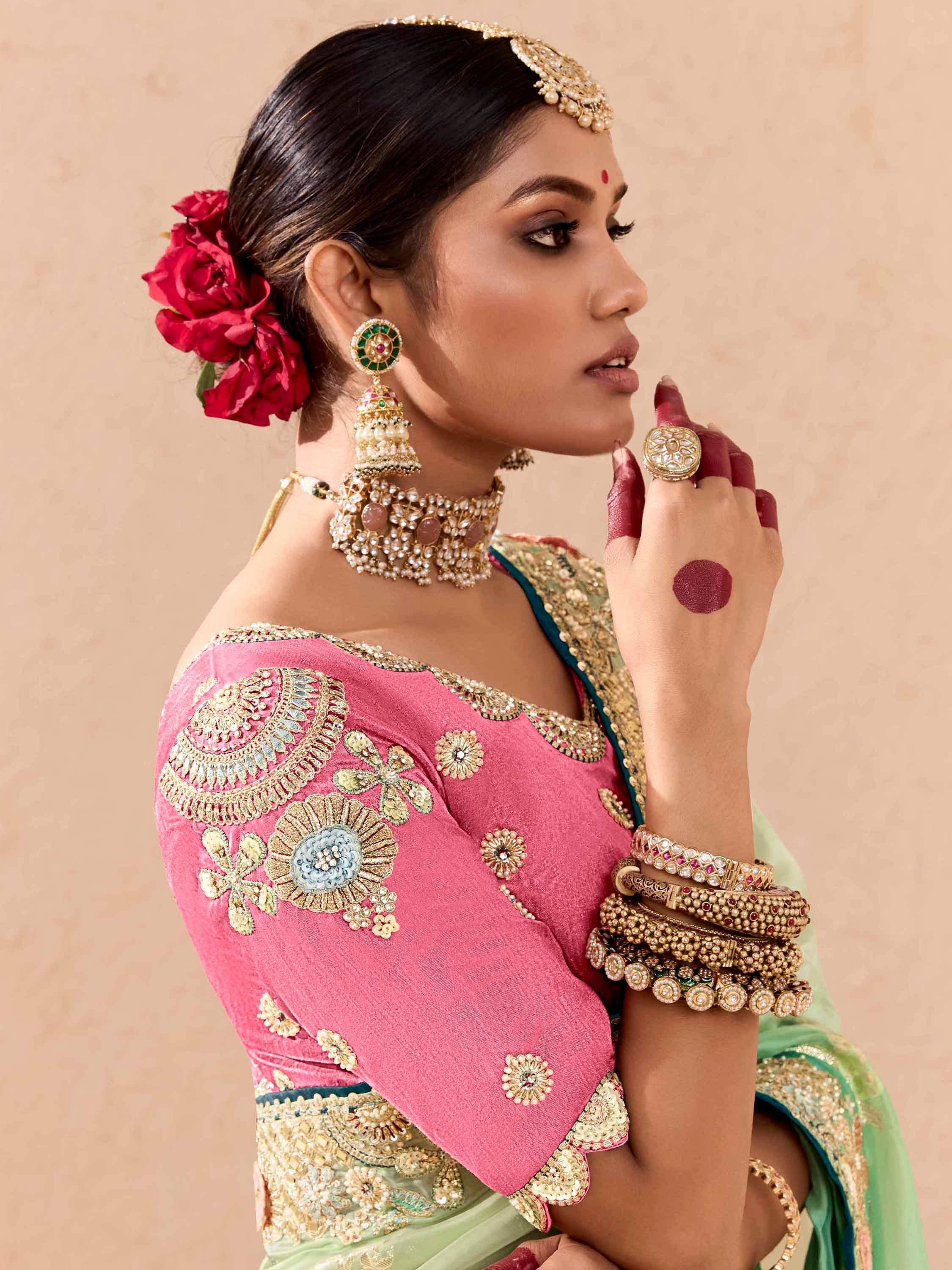 Woman in pink embroidered blouse and green saree with traditional Indian jewelry and red flowers in hair