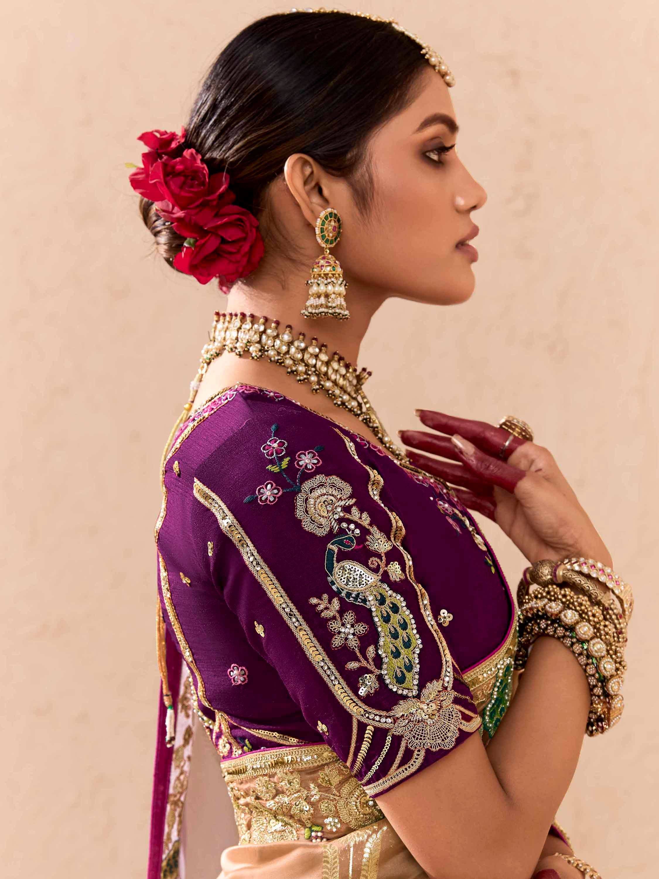 Elegant woman in purple embroidered lehenga choli with peacock design, gold jewelry, and red floral hair accessory