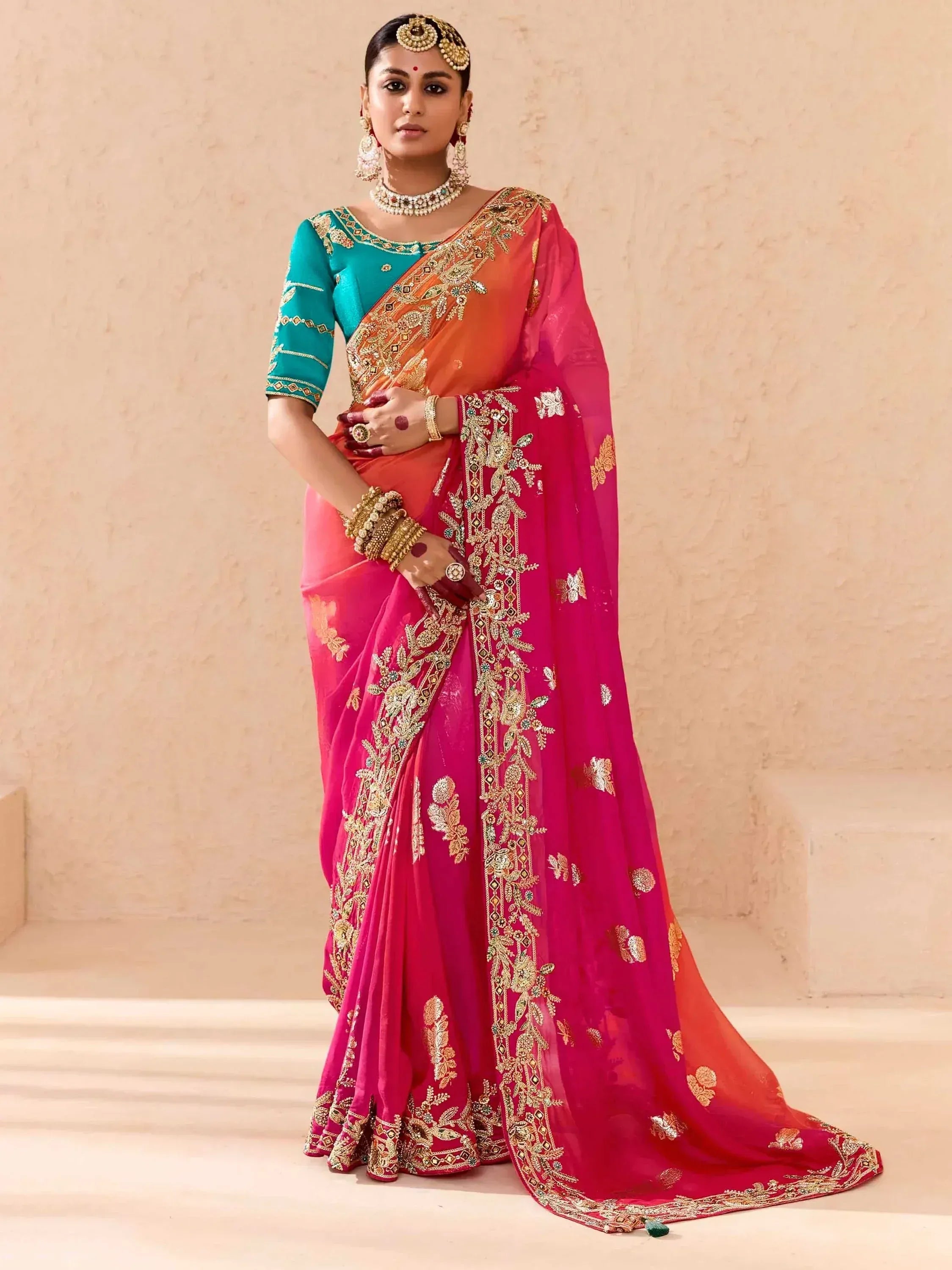 Woman in vibrant pink and orange embroidered saree with teal blouse, traditional Indian ethnic wear