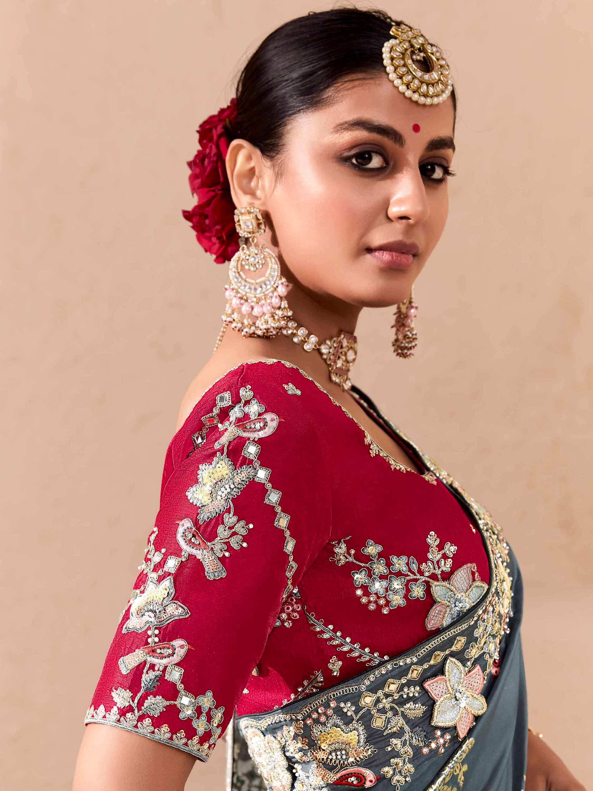 Elegant woman in red embroidered saree with floral motifs, gold jewelry, and traditional Indian headpiece