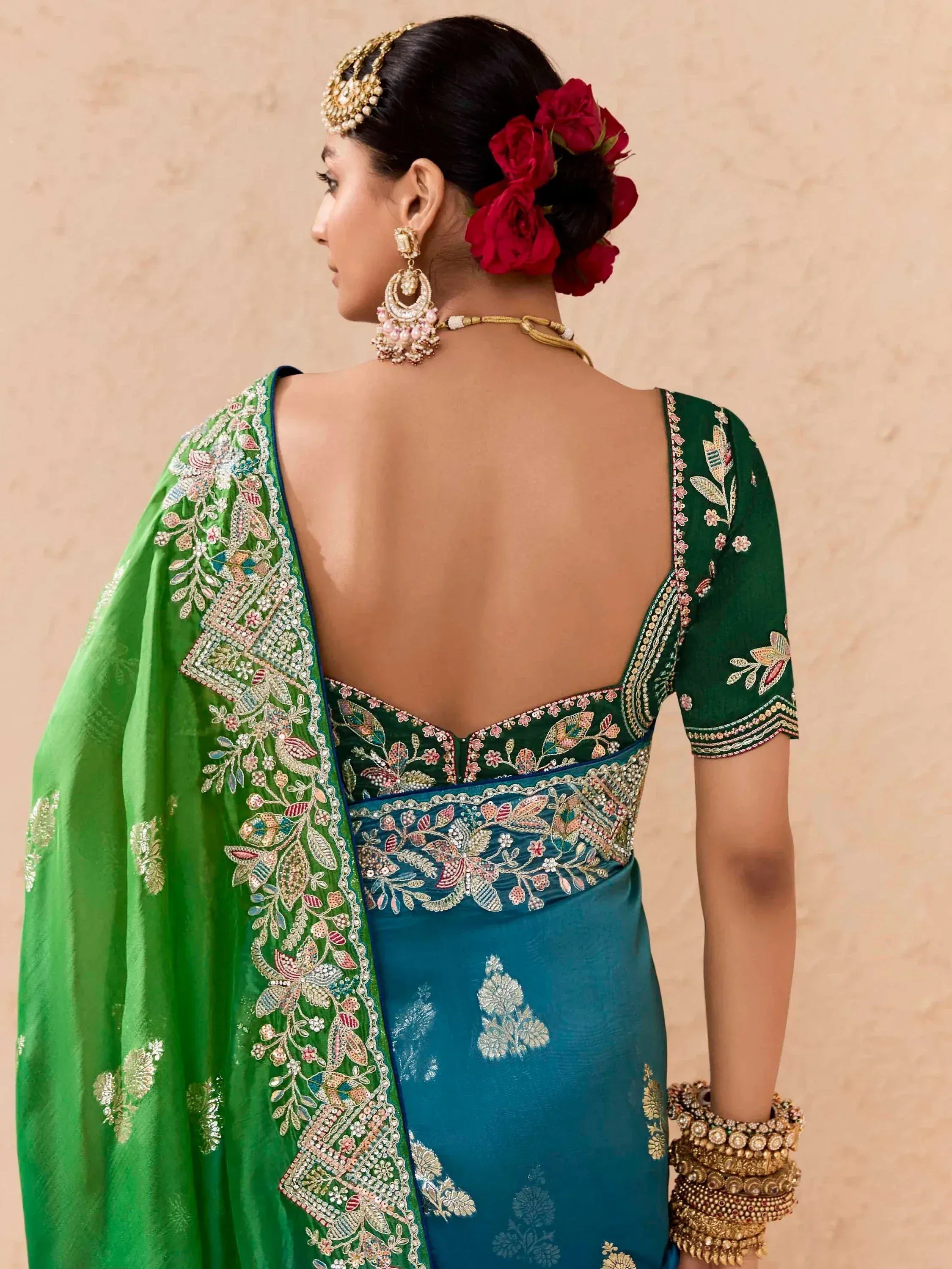 Green and teal embroidered saree with open back, floral jewelry, and red rose hair accessory