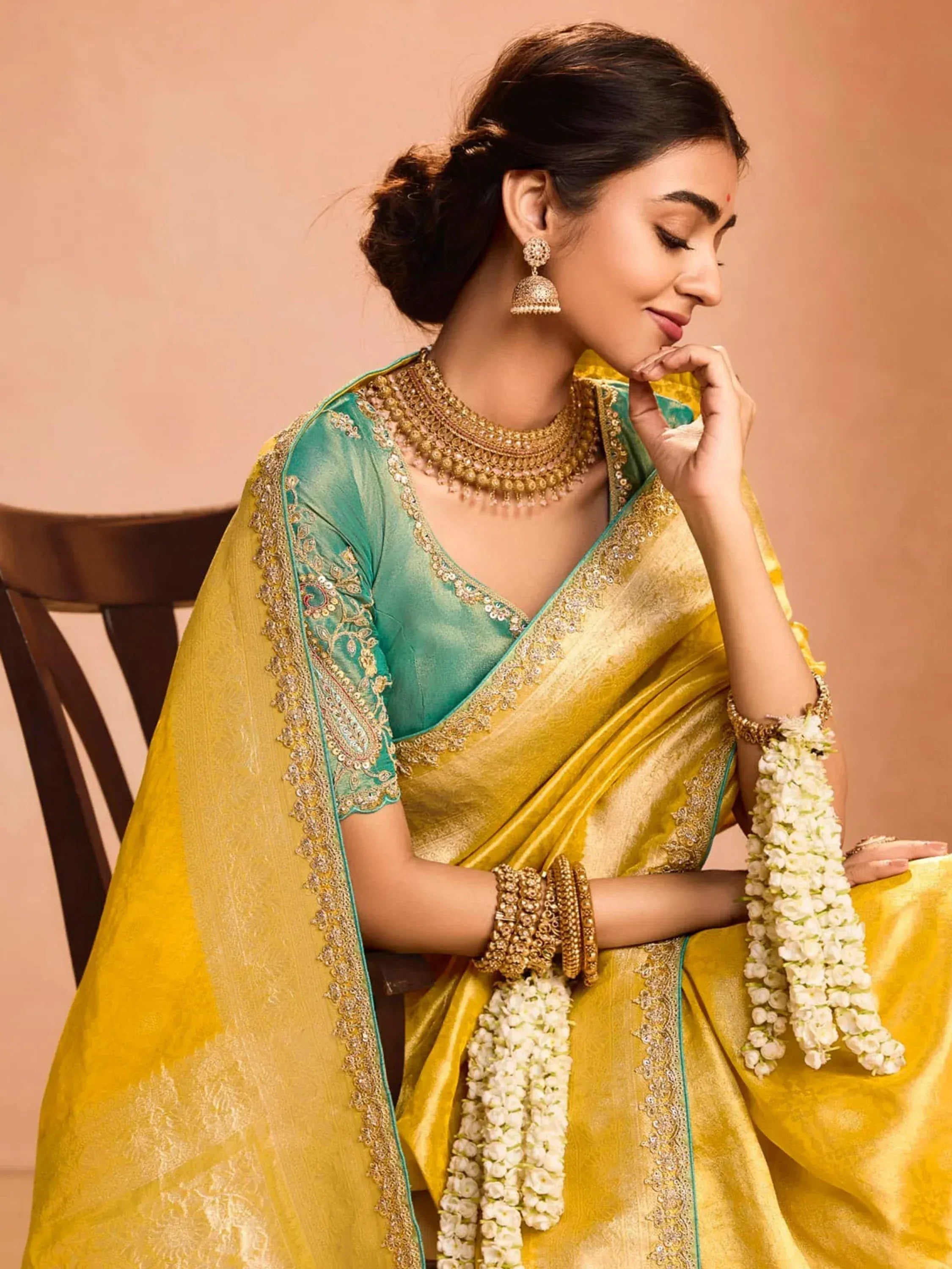 Woman in elegant yellow and green saree with gold embroidery, traditional jewelry, and floral garlands