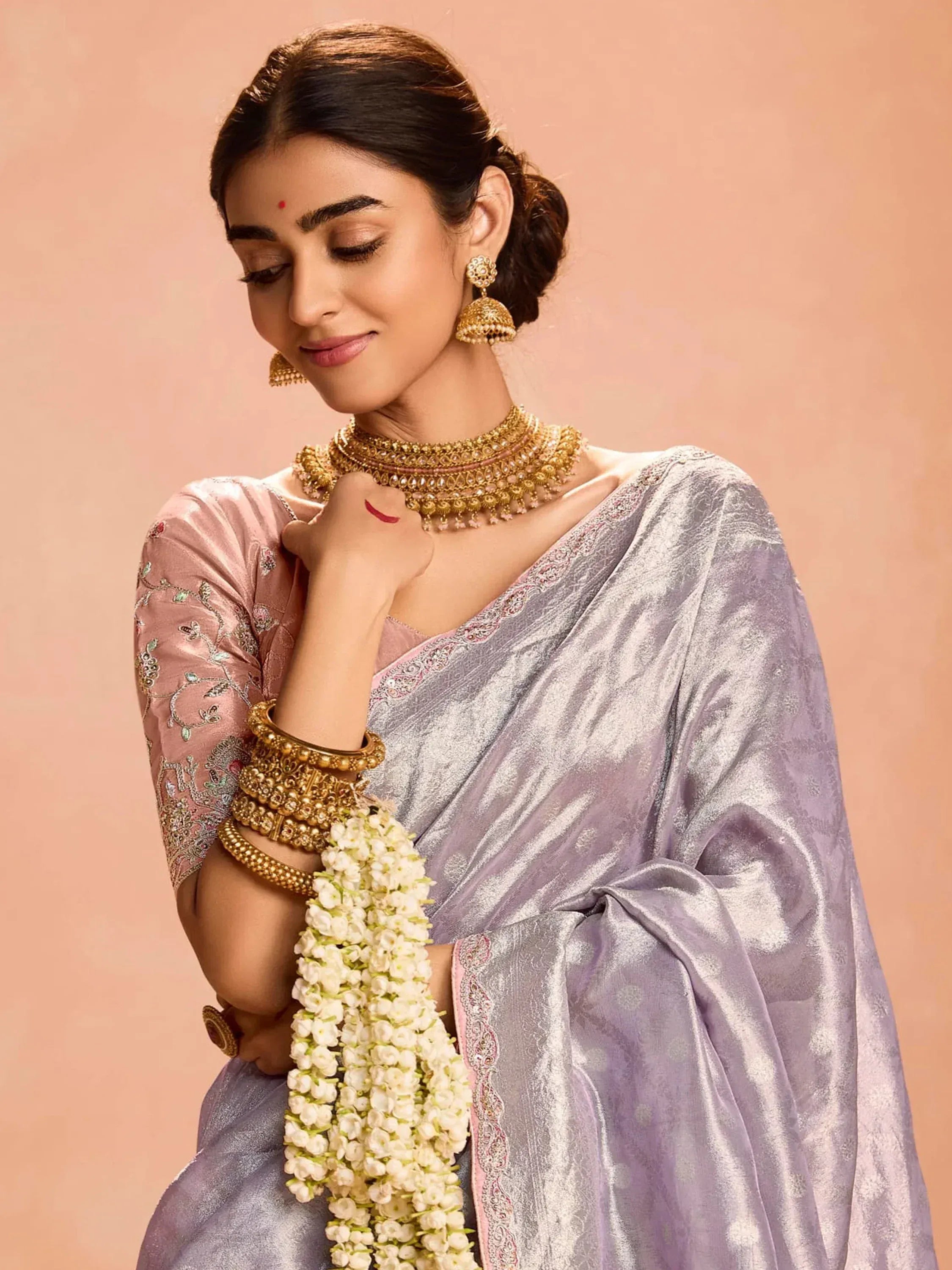 Elegant woman in lavender saree with gold jewelry and floral garland, showcasing Indian ethnic wear