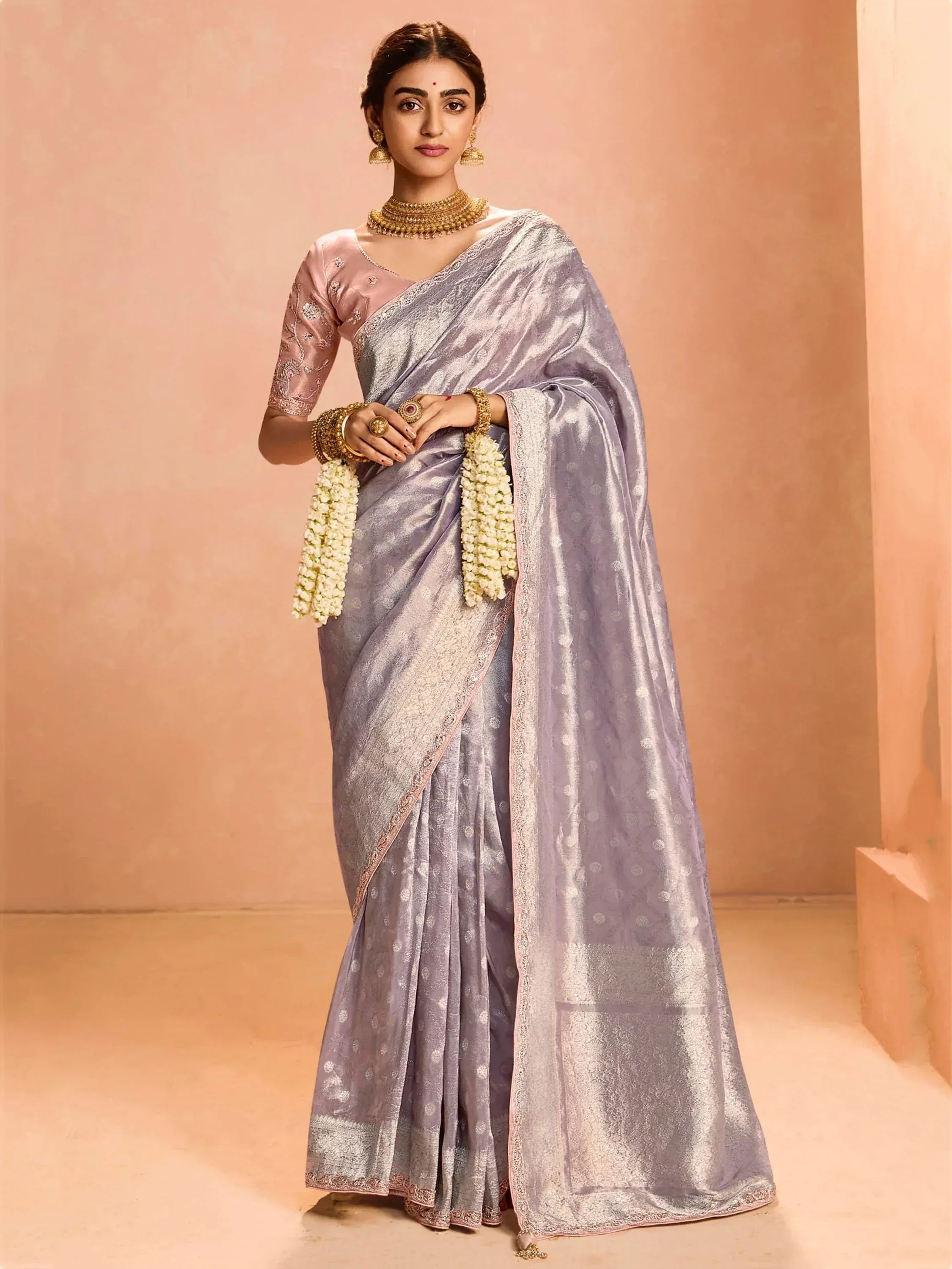 Elegant lavender silk saree with gold embroidery, paired with pink blouse and traditional jewelry for Indian ethnic wear.