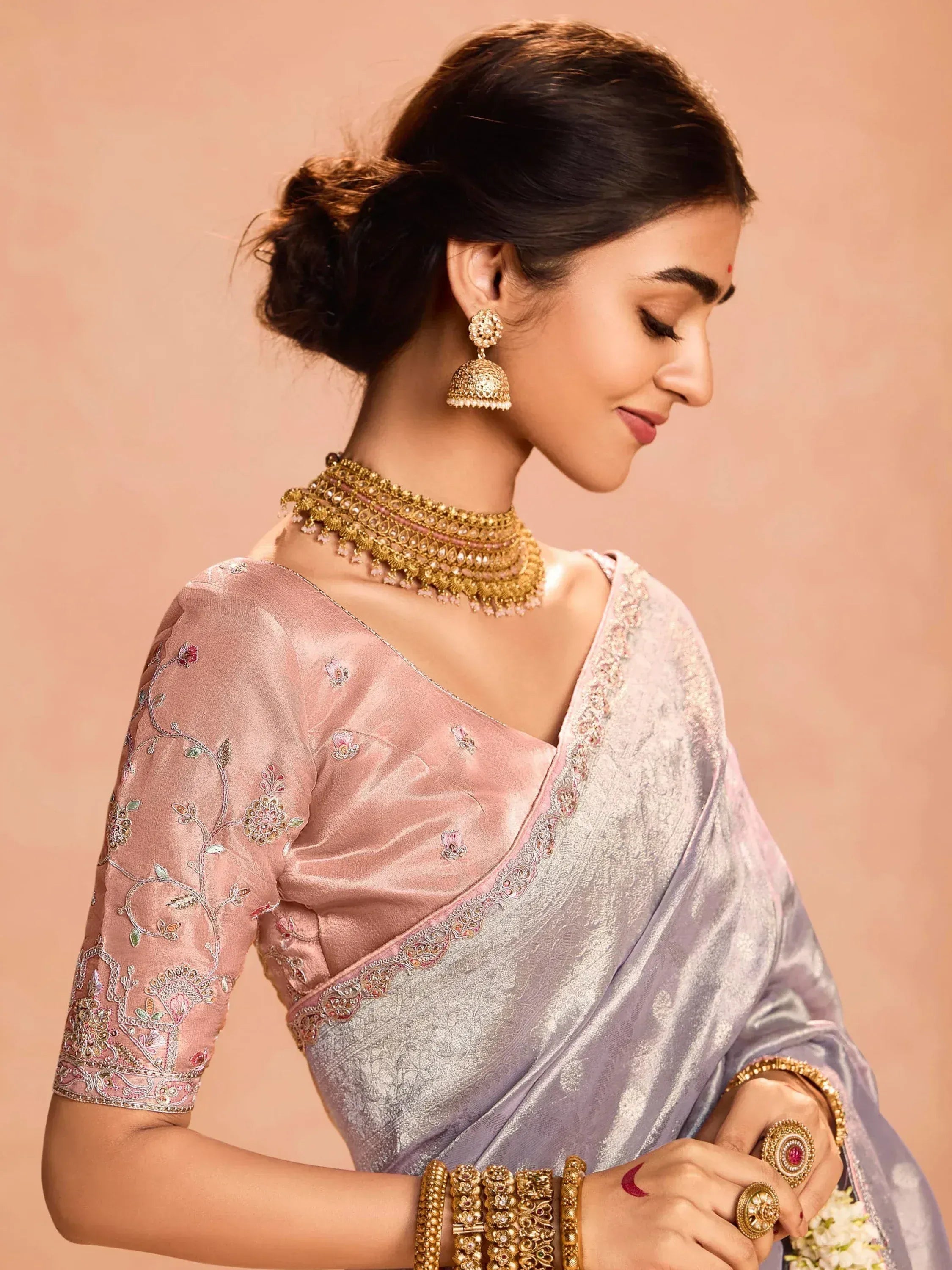 Elegant woman in pink embroidered blouse and silver saree with gold jewelry, showcasing Indian ethnic wear