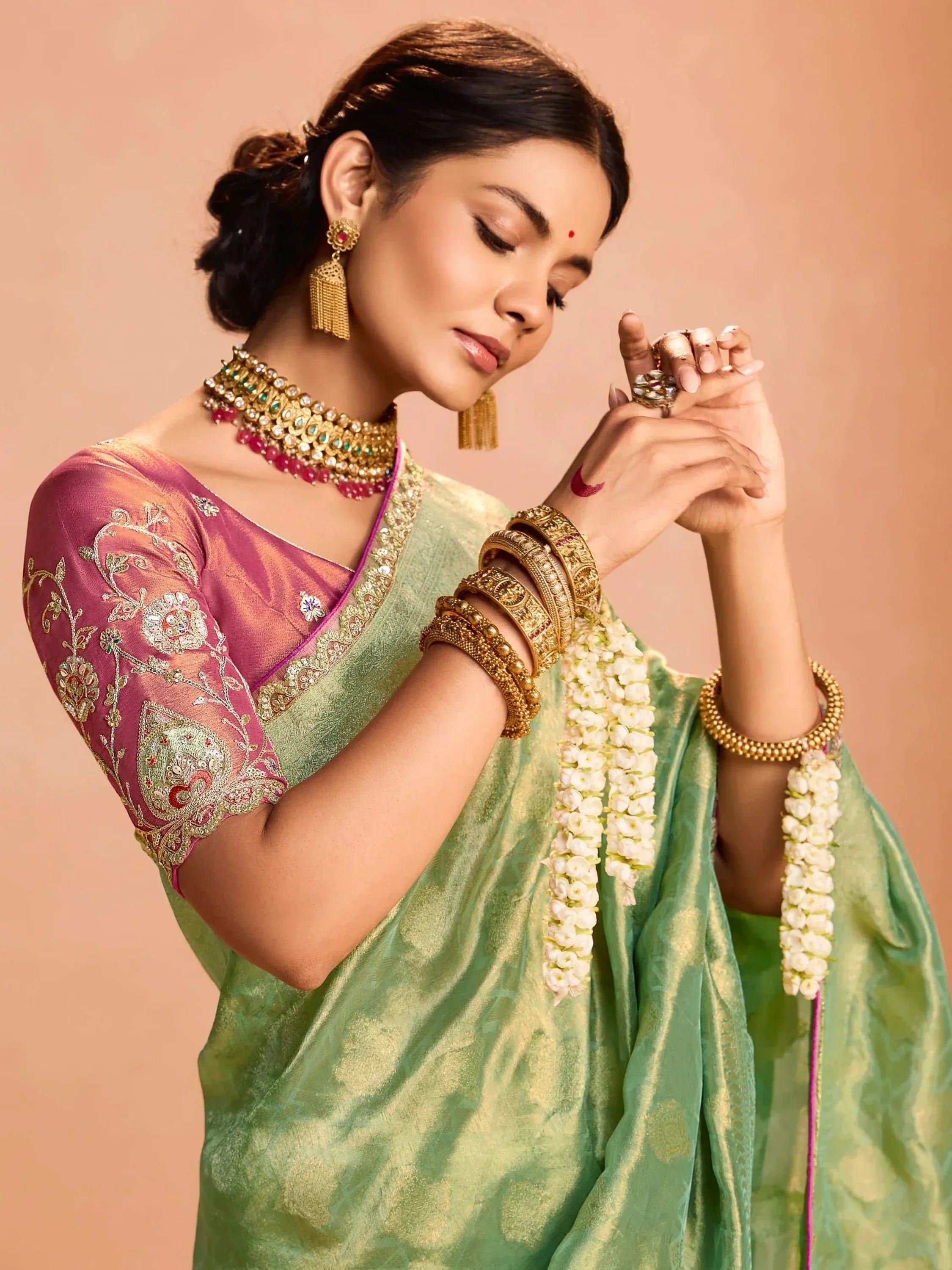 Woman in green saree with pink embroidered blouse, gold jewelry, and floral garlands for Indian ethnic wear