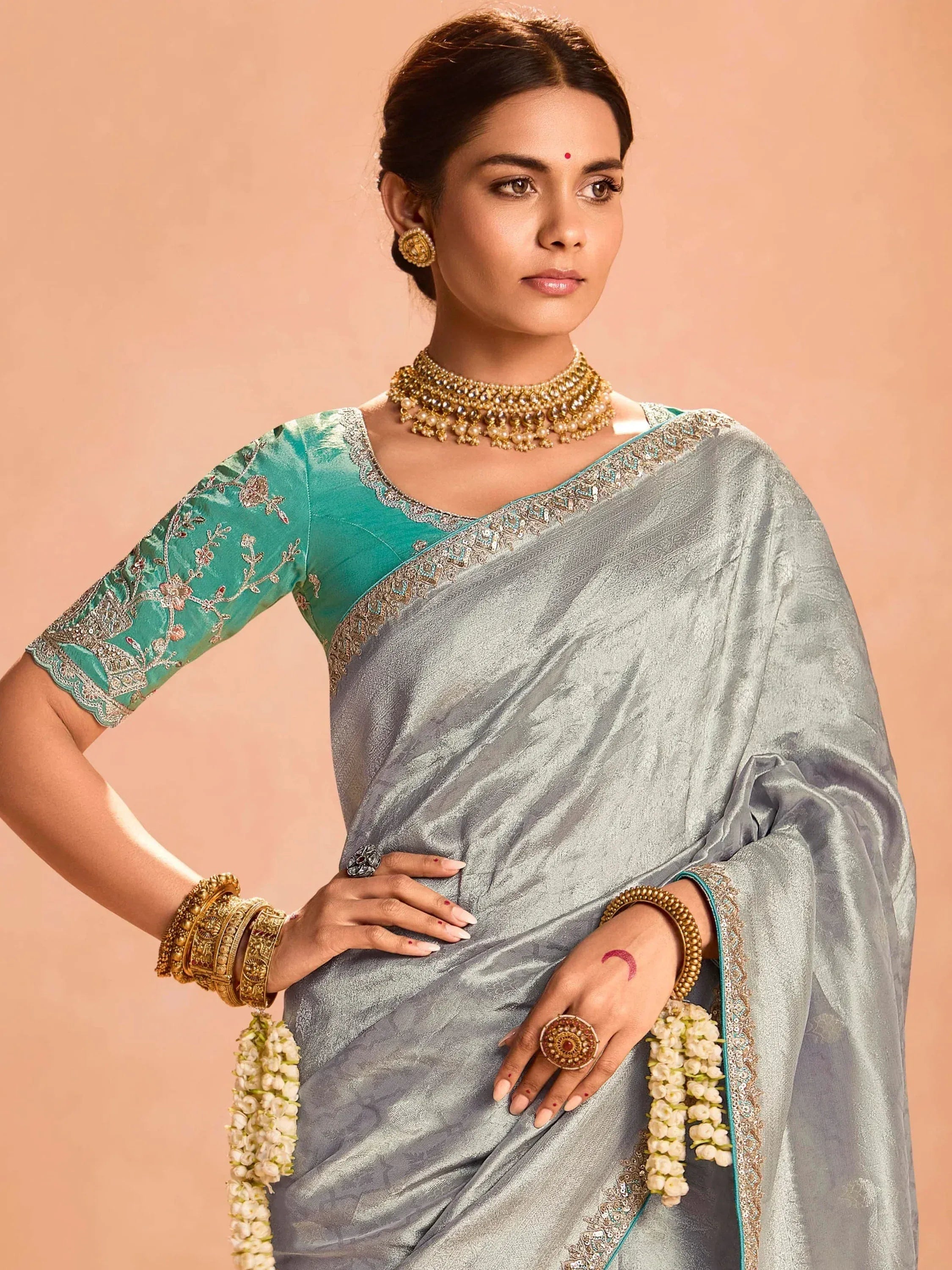 Elegant silver saree with teal blouse, gold jewelry, and floral accents for Indian ethnic wear