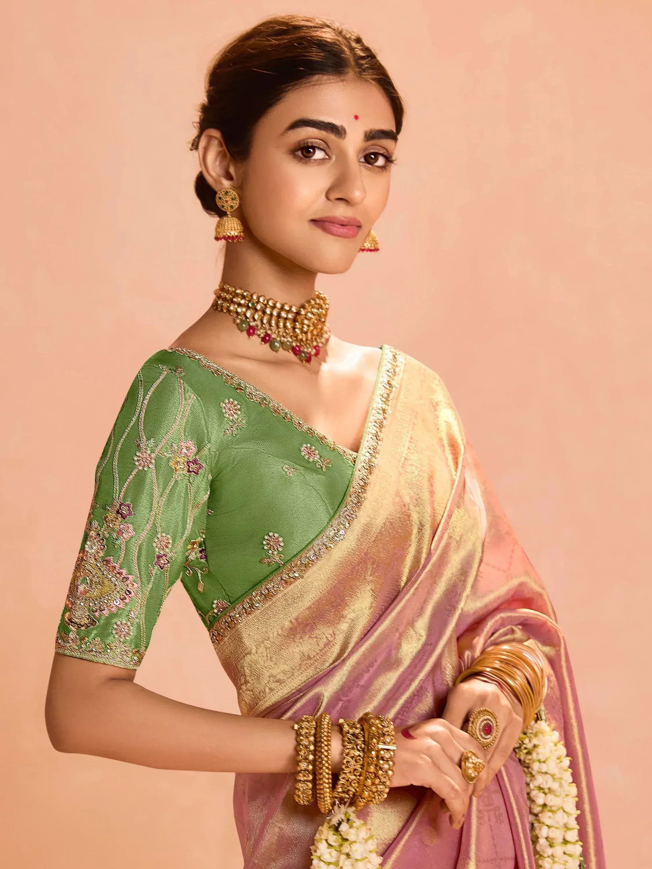 Elegant woman in green embroidered blouse and pink saree with gold jewelry
