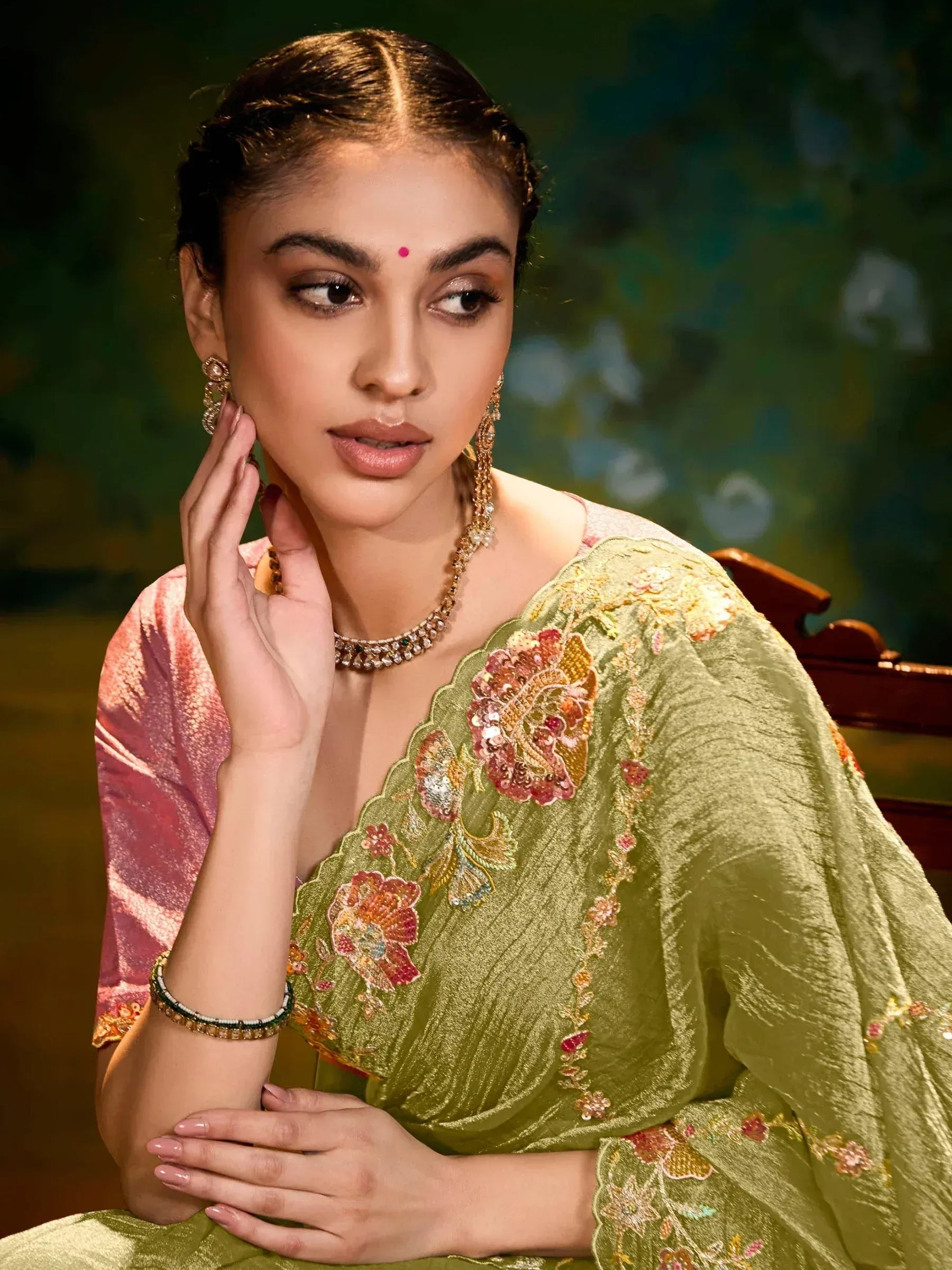 Woman in olive green embroidered saree with floral motifs, paired with pink blouse and traditional jewelry